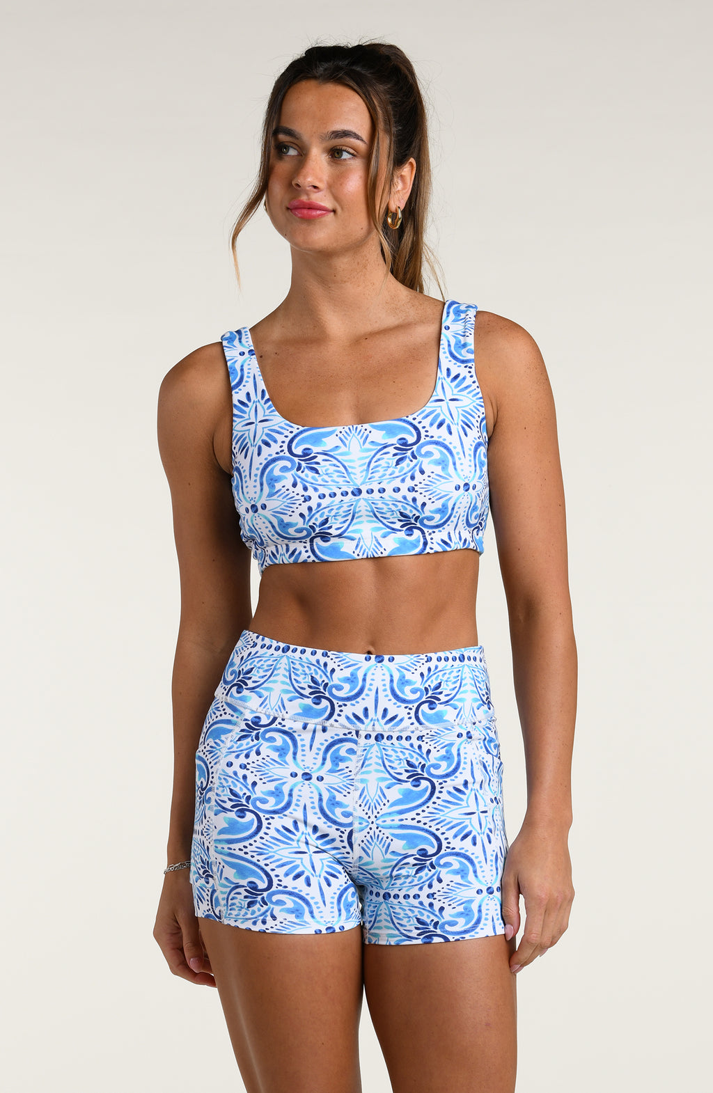 Woman wearing a blue and white multicolored patterned sports bra and matching bike shorts worn by a person on a beige background