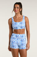 Woman wearing a blue and white multicolored patterned sports bra and matching bike shorts worn by a person on a beige background