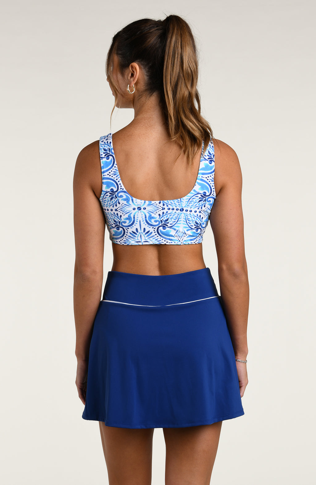 Woman wearing a blue and white multicolored patterned sports bra and navy colored bike shorts worn by a person on a beige background