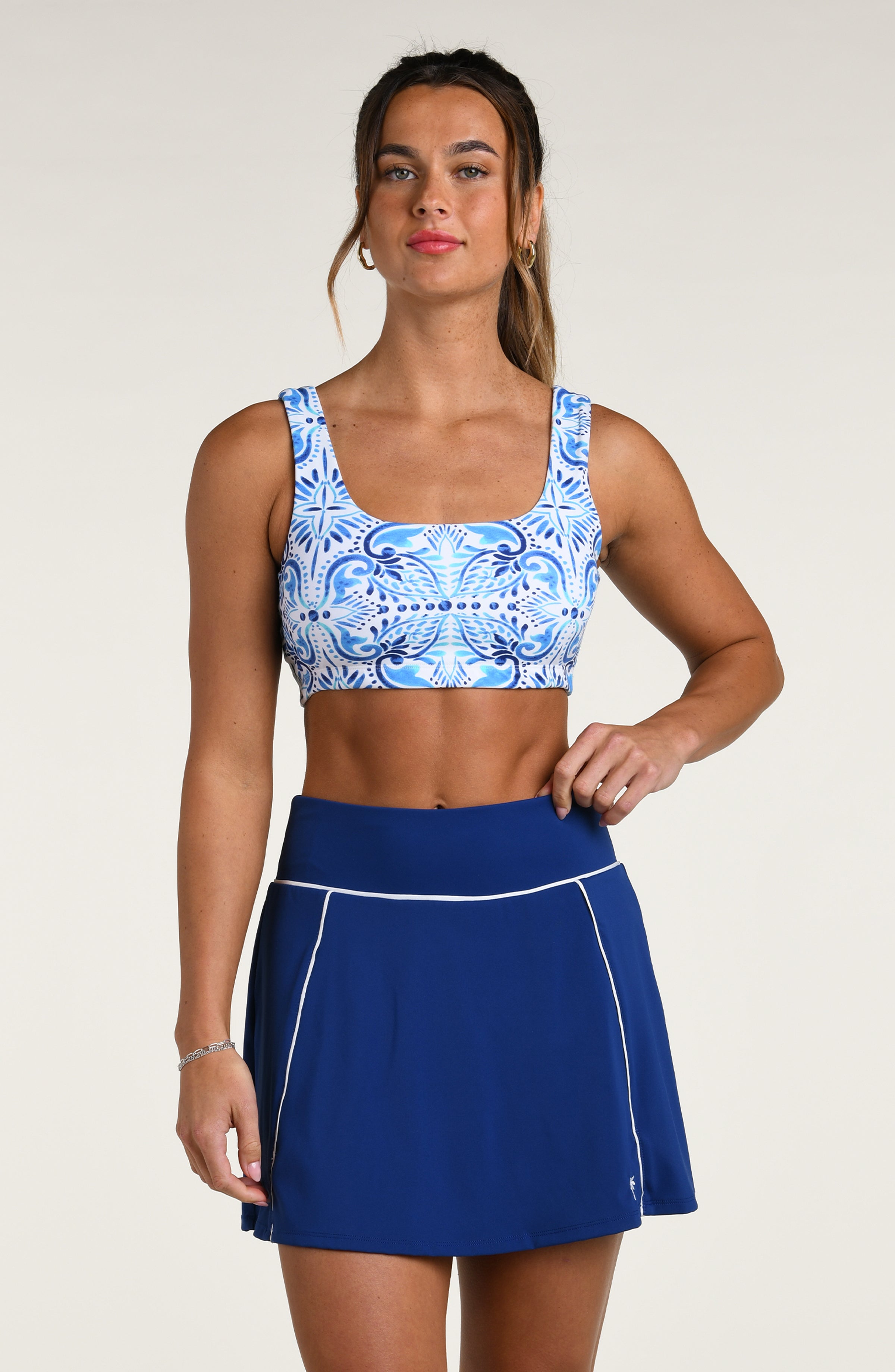 Woman wearing a blue and white multicolored sports bra and navy blue skort against a white background.