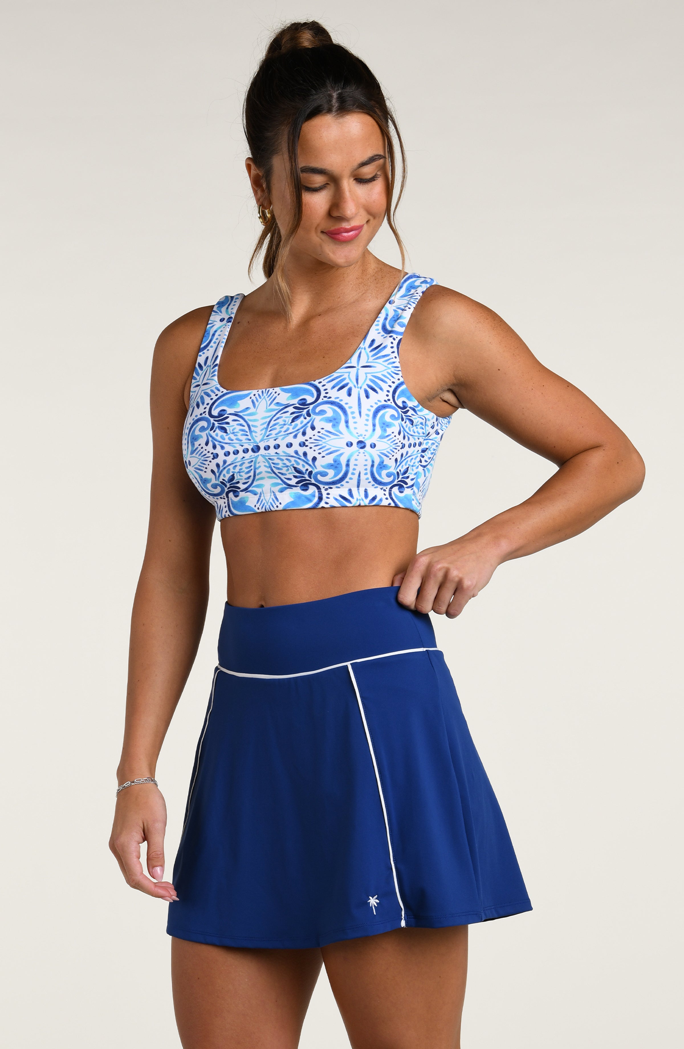 Woman wearing a blue and white patterned sports bra and blue active skorts against a white background