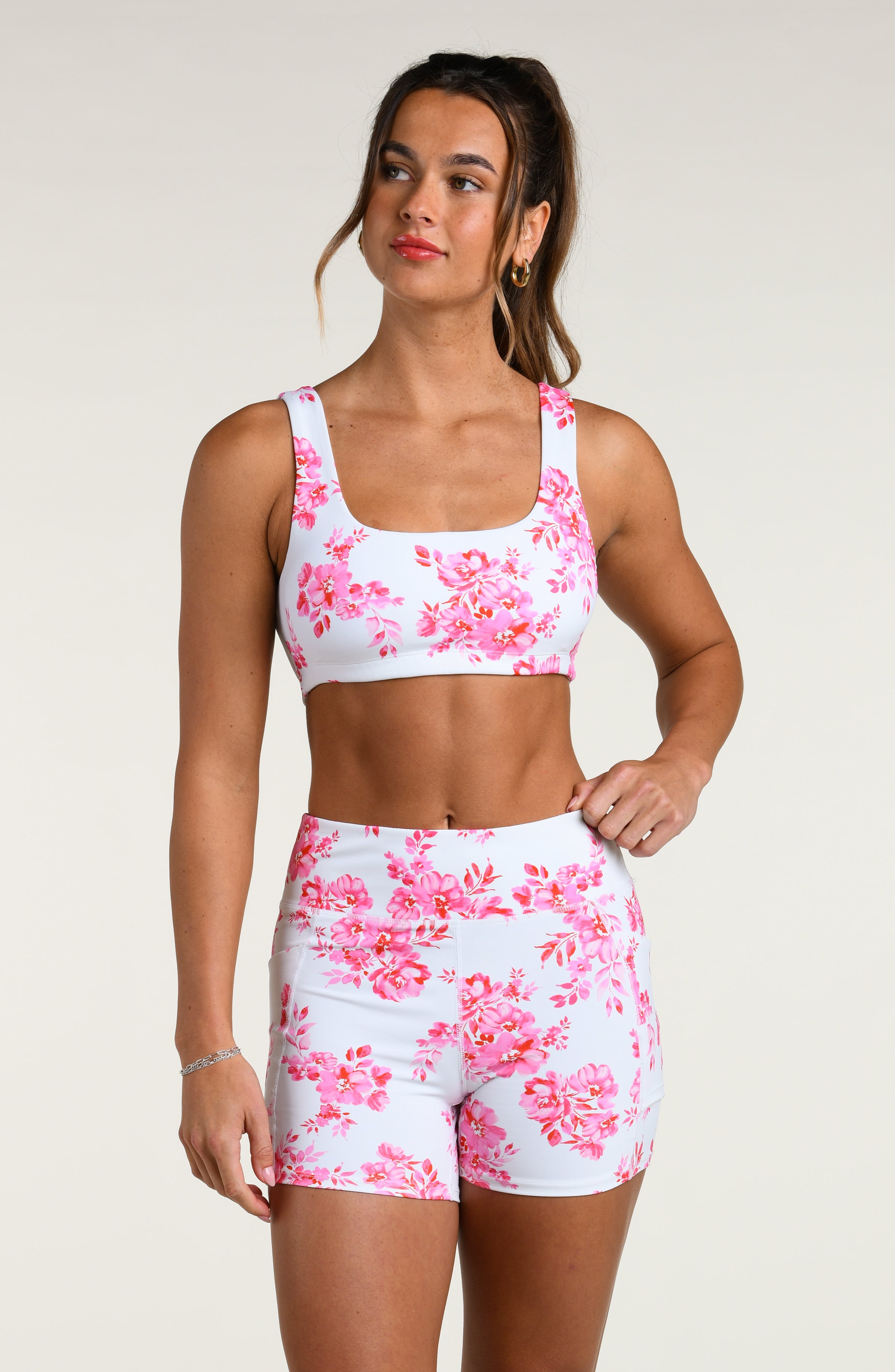 Woman wearing a pink floral sports bra and matching biker shorts set on a white background