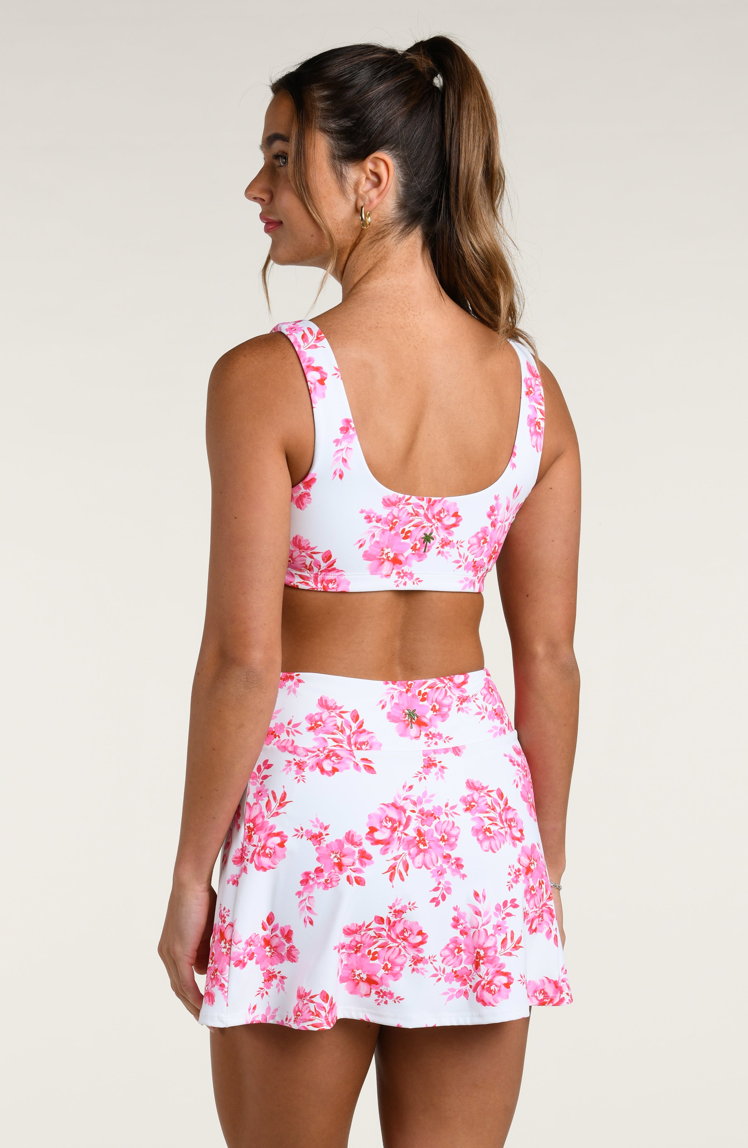Woman wearing a pink floral sports bra and matching skort set on a white background