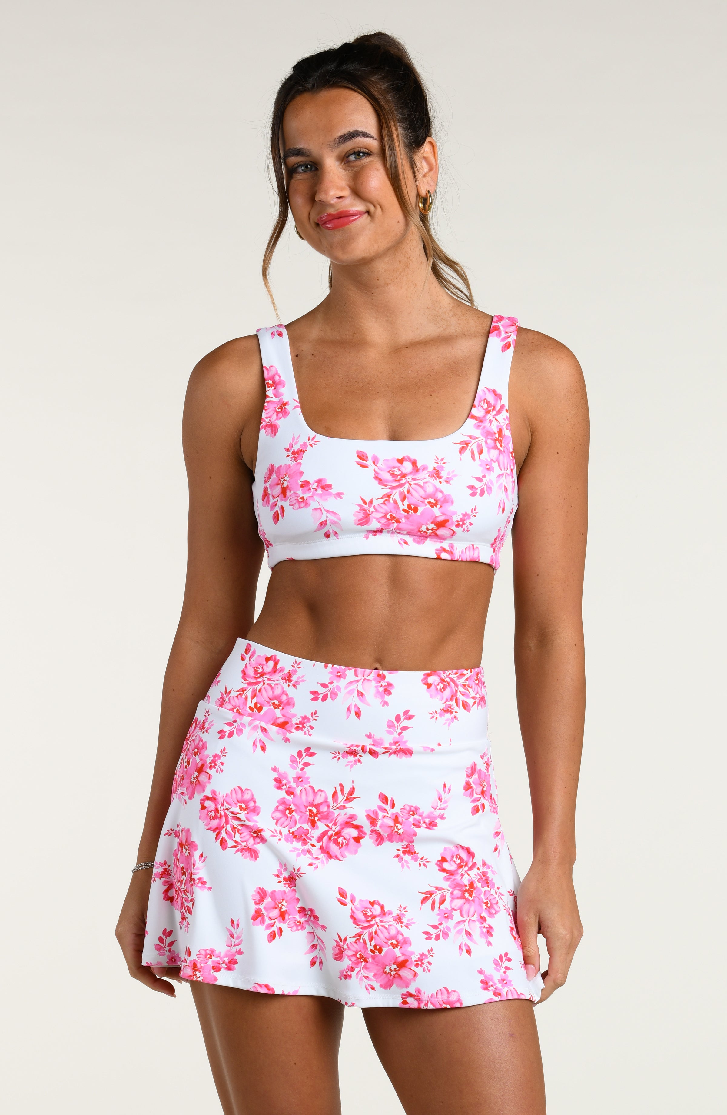 Woman wearing a pink floral sports bra and matching skort set on a white background