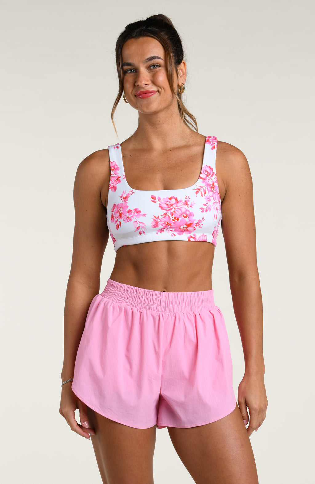 Woman wearing a pink floral sports bra and pink shorts on a white background