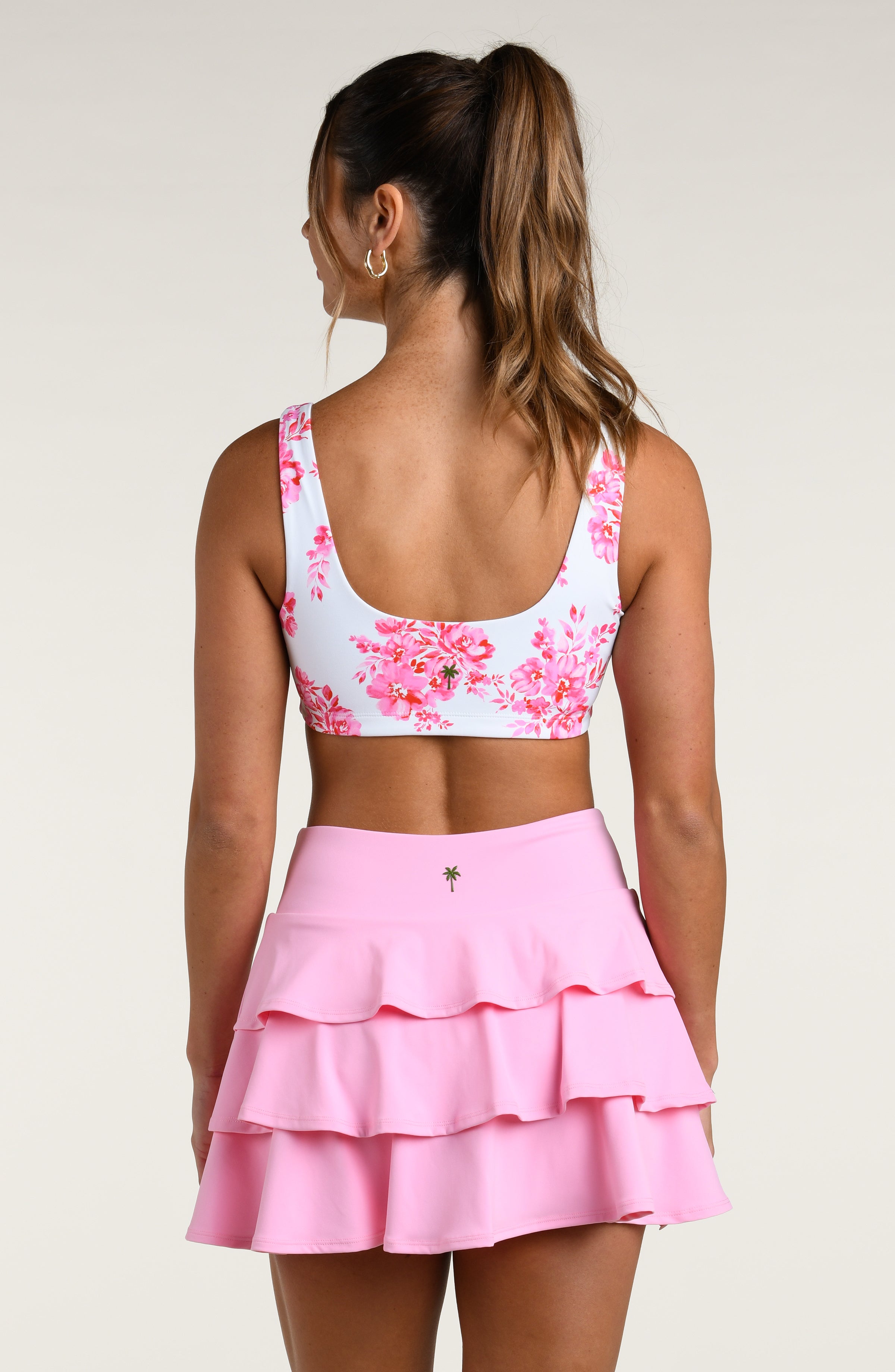 Woman wearing a floral sports bra and pink skort on a white background
