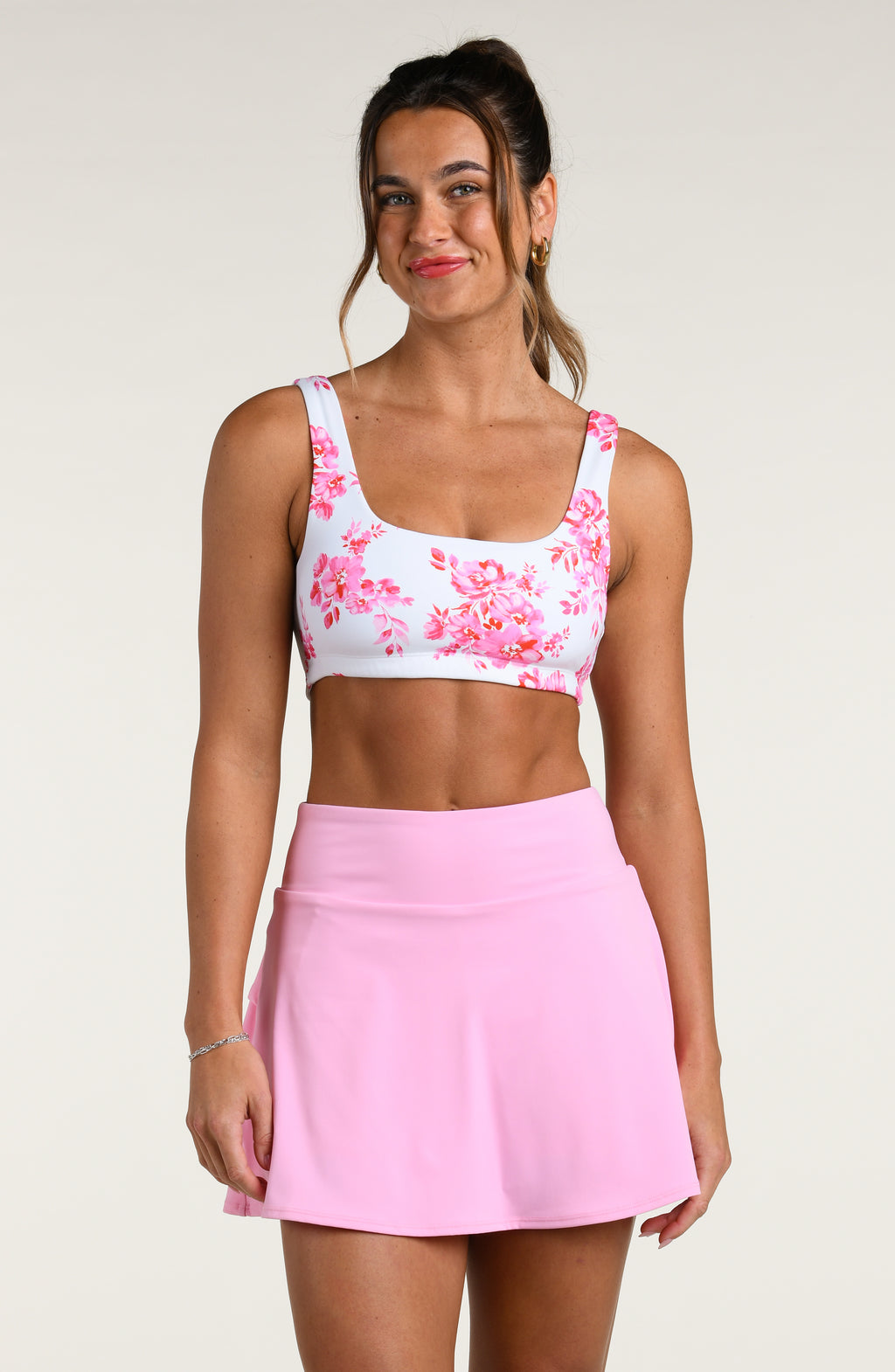 Woman wearing a pink floral sports bra and pink skort set on a white background