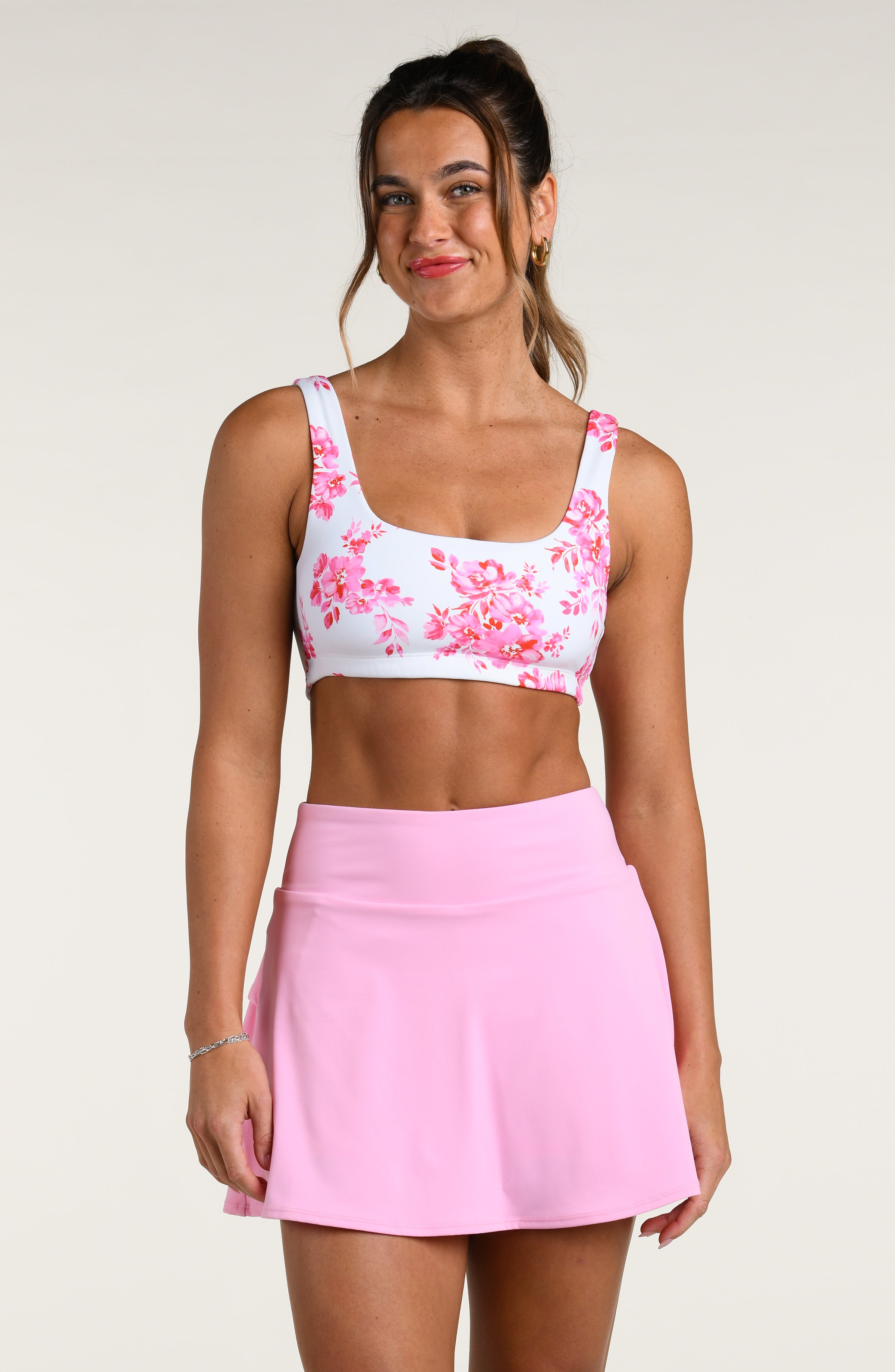 Woman wearing a pink floral sports bra and pink skort set on a white background