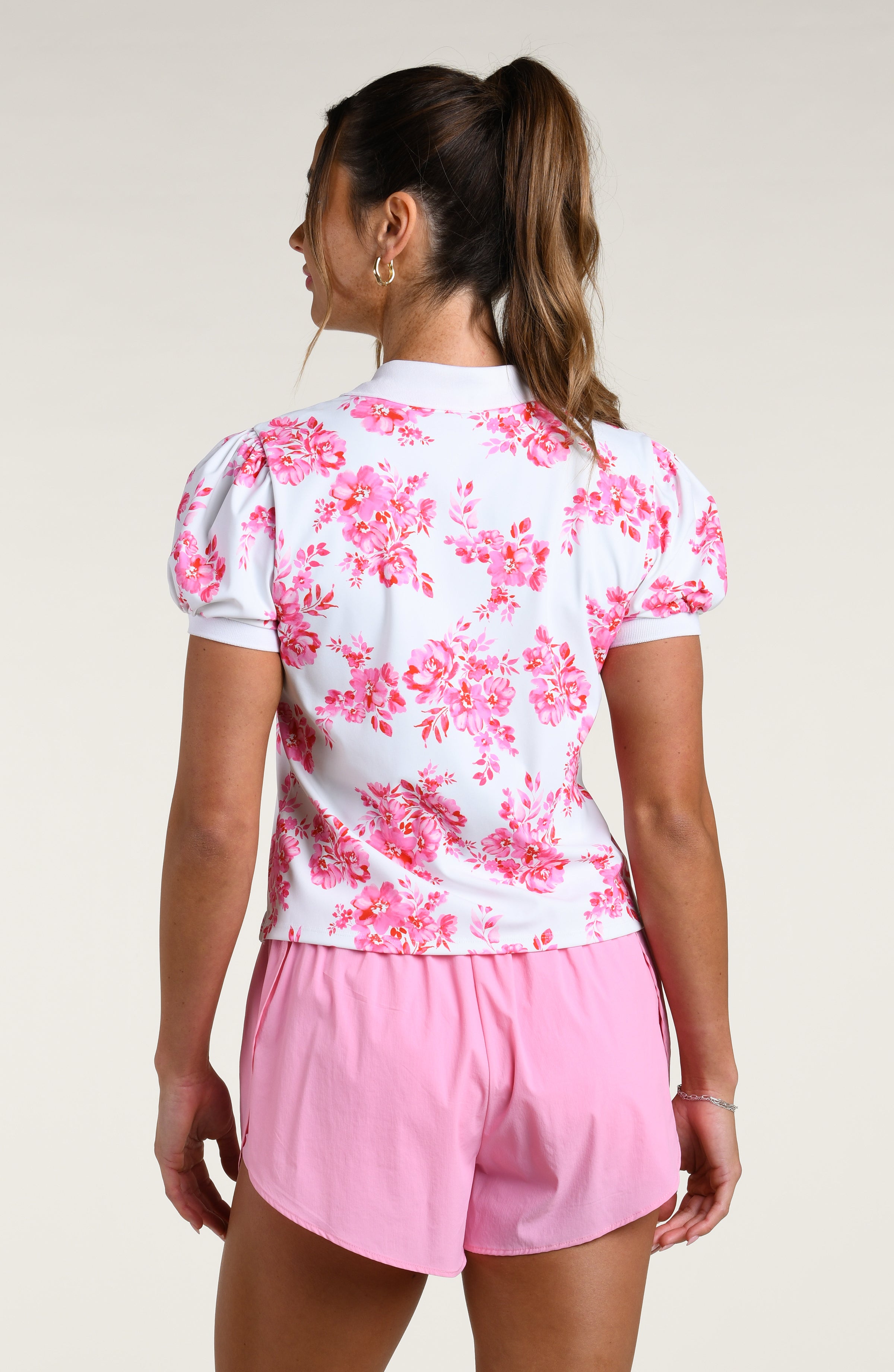 Woman wearing a pink floral polo shirt and pink shorts on a plain background