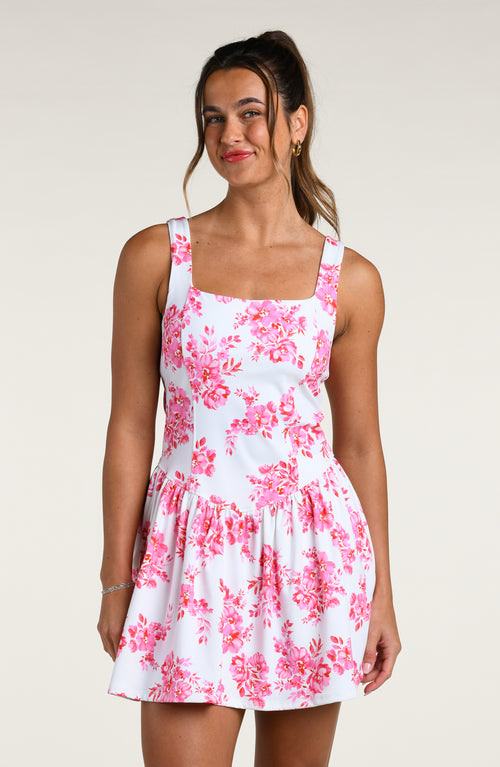 Woman wearing a pink and white floral dress against a white background. 