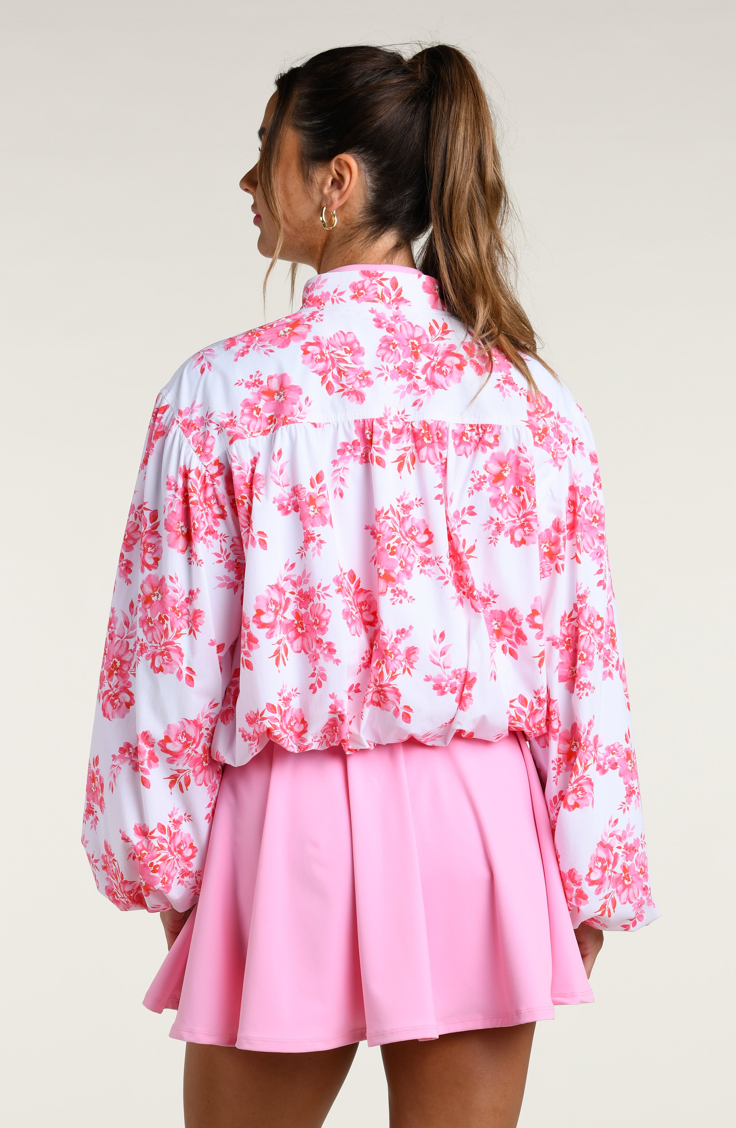 Woman wearing a pink floral jacket and pink tennis dress on a white background