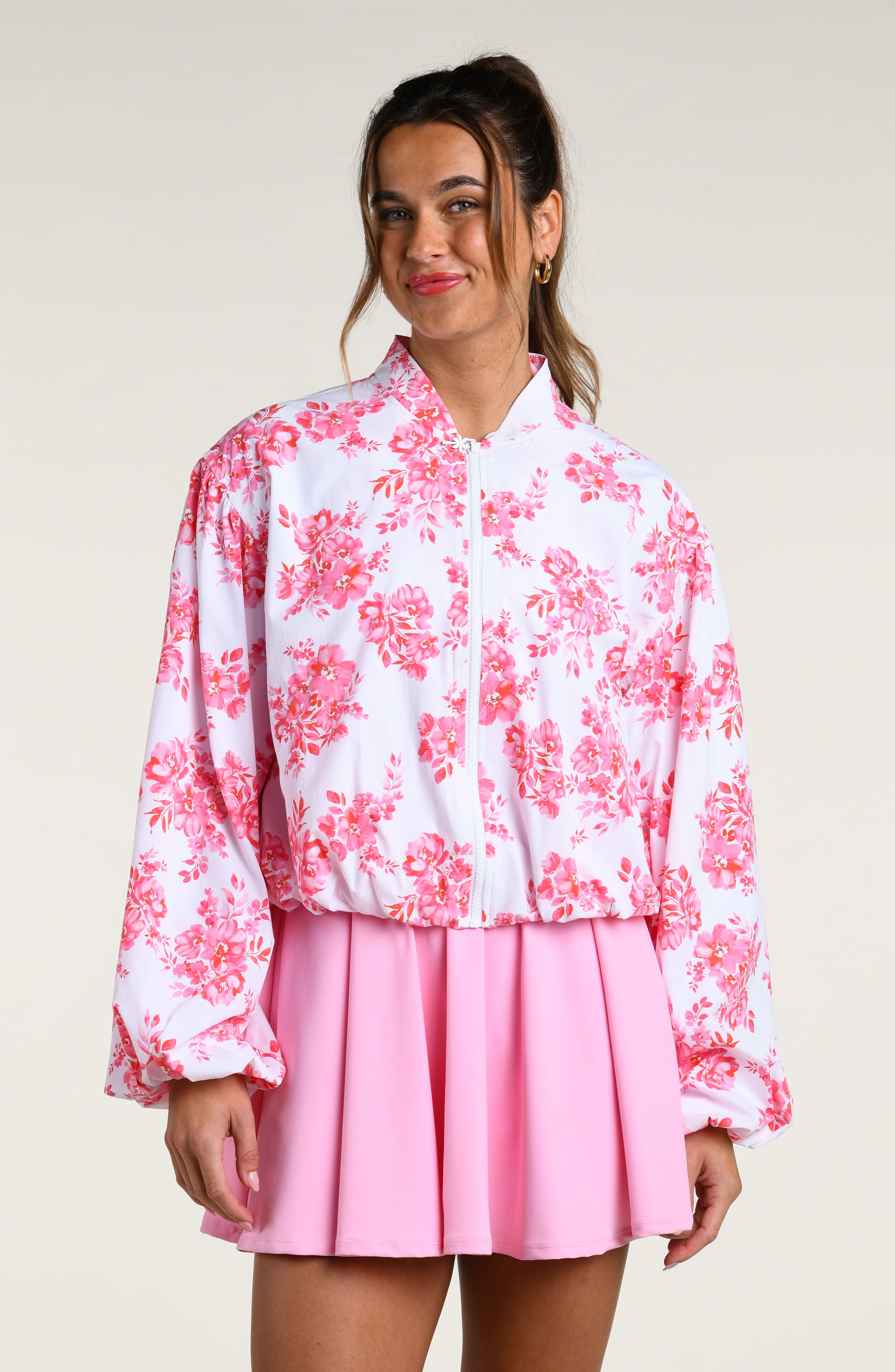 Woman wearing a pink floral jacket and pink tennis dress on a white background