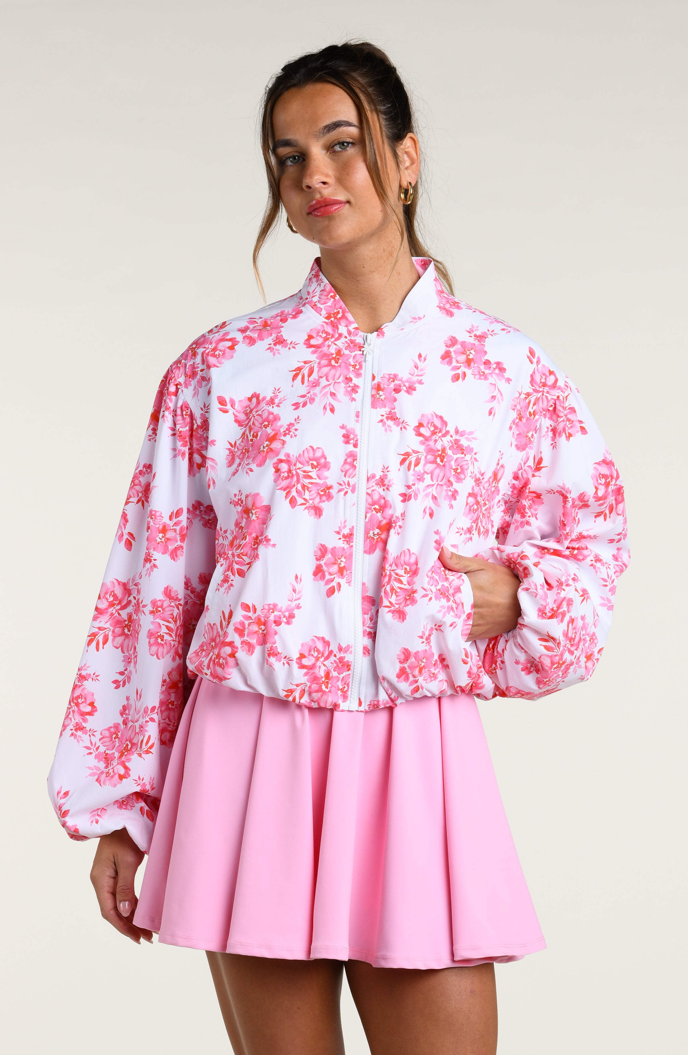Woman wearing a pink floral jacket and pink tennis dress on a white background