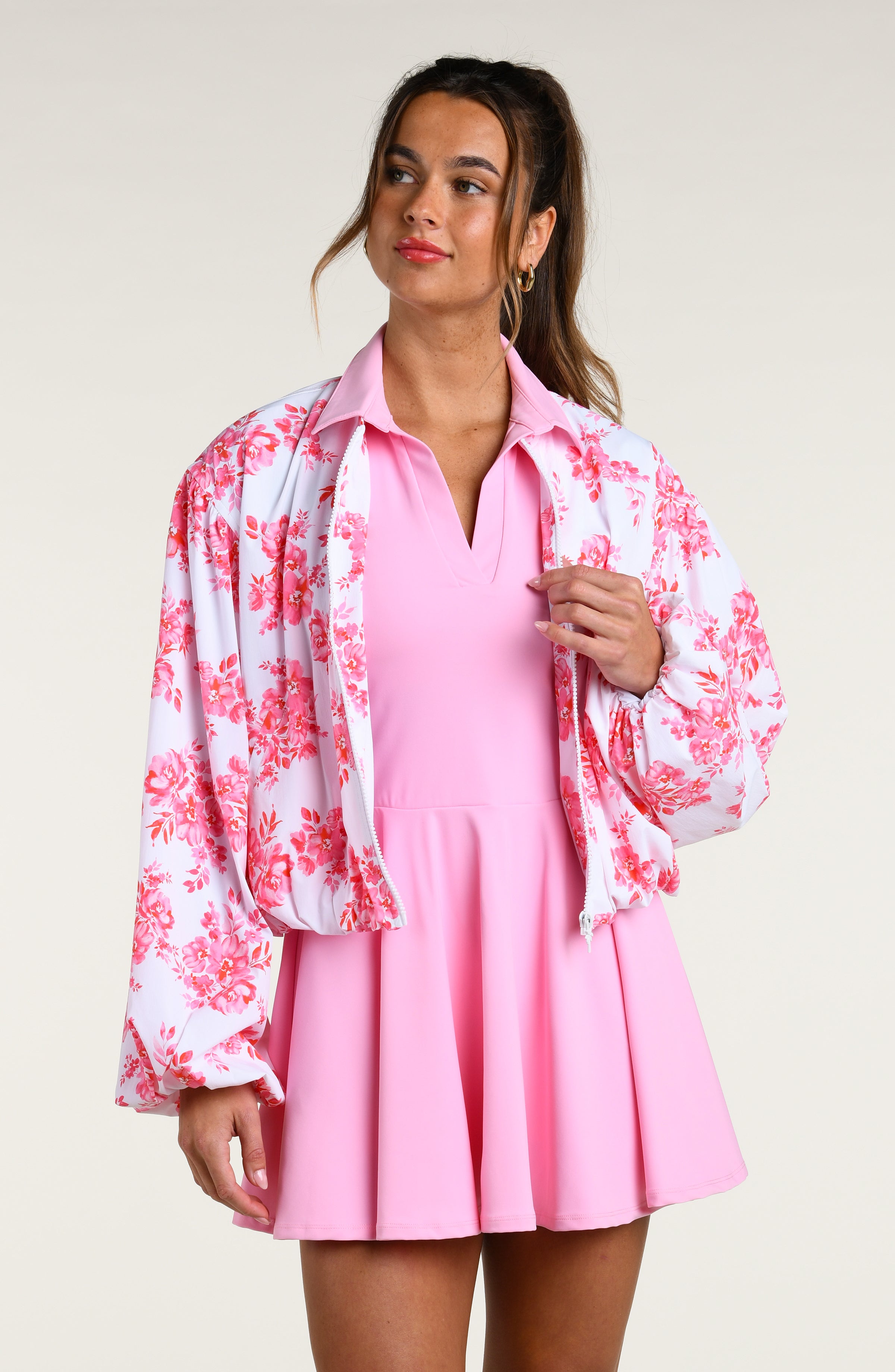 Woman wearing a pink floral jacket and pink tennis dress on a white background