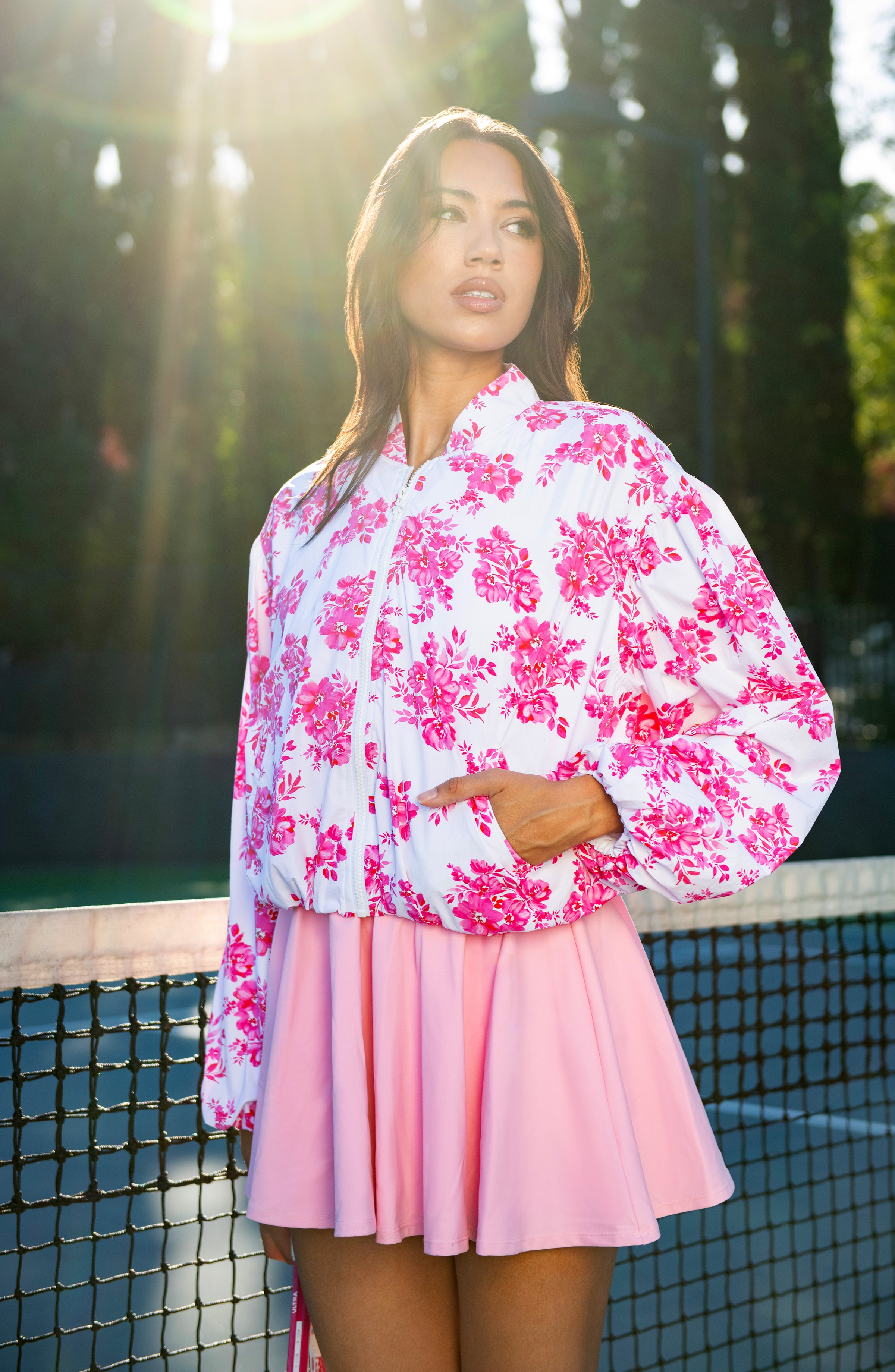 Woman wearing a pink floral jacket and tennis dress on a tennis court