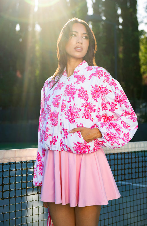 Woman wearing a pink floral jacket and tennis dress on a tennis court