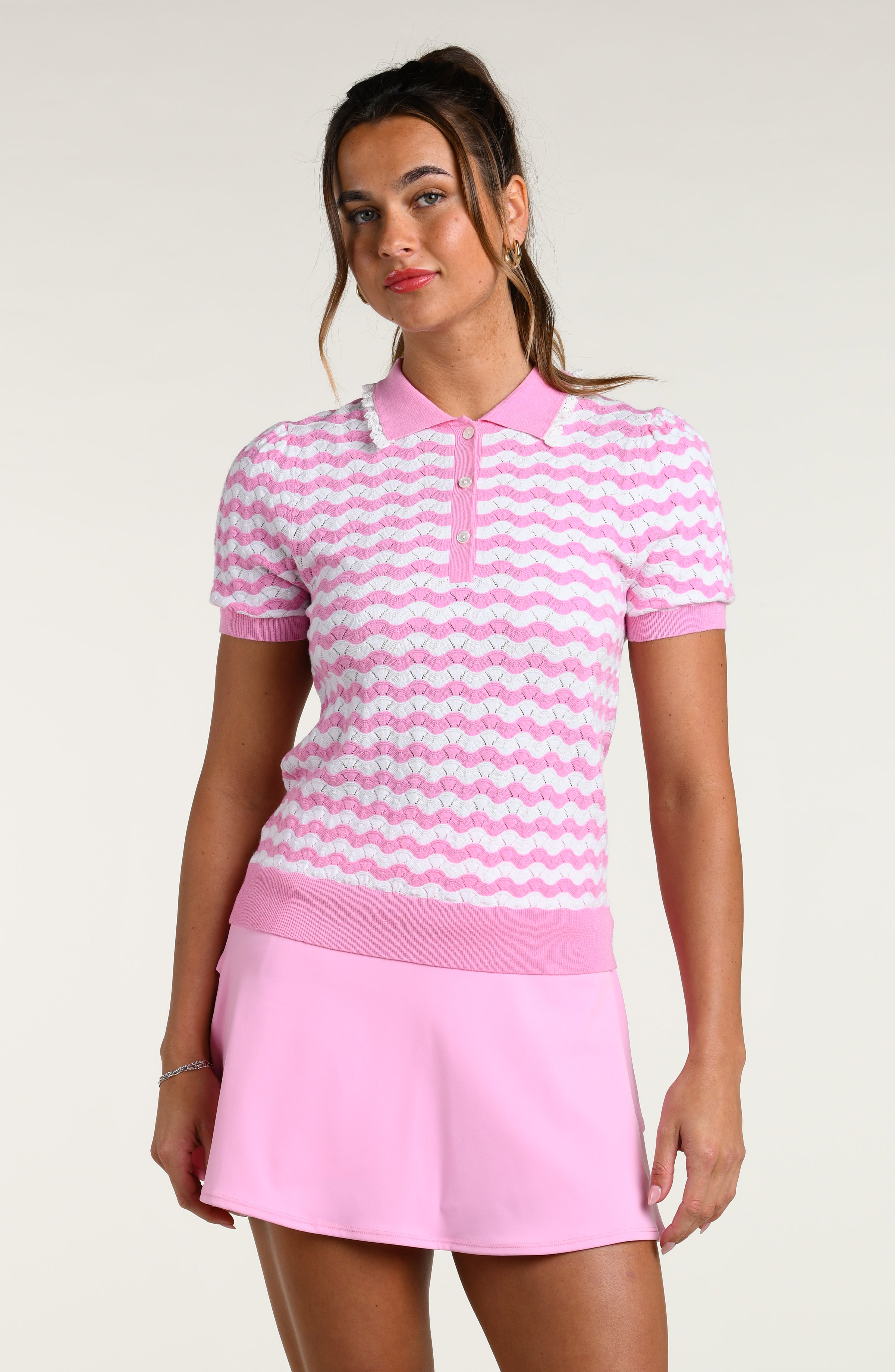 Woman wearing a pink and white striped polo shirt and pink skort on a white background