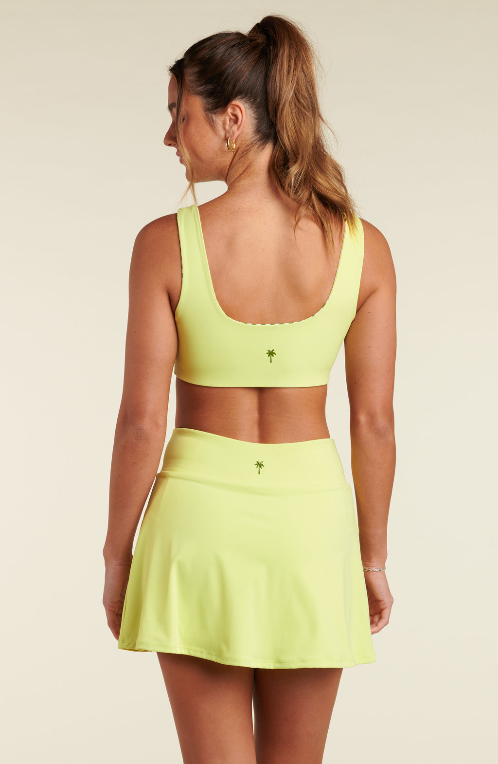 Woman wearing a lime green sports bra and matching skort against a beige background