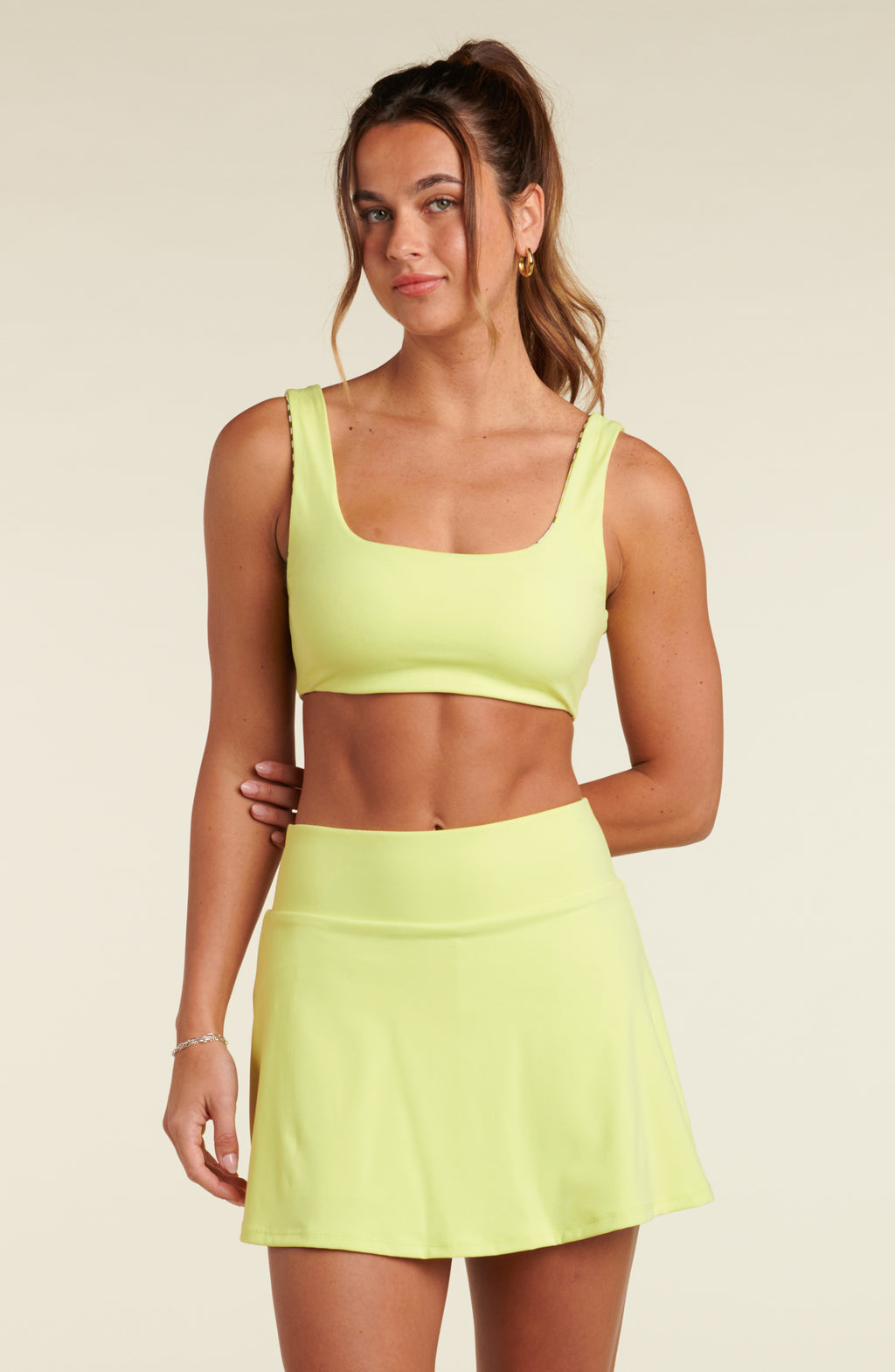 Woman wearing a lime green sports bra and matching skort against a beige background