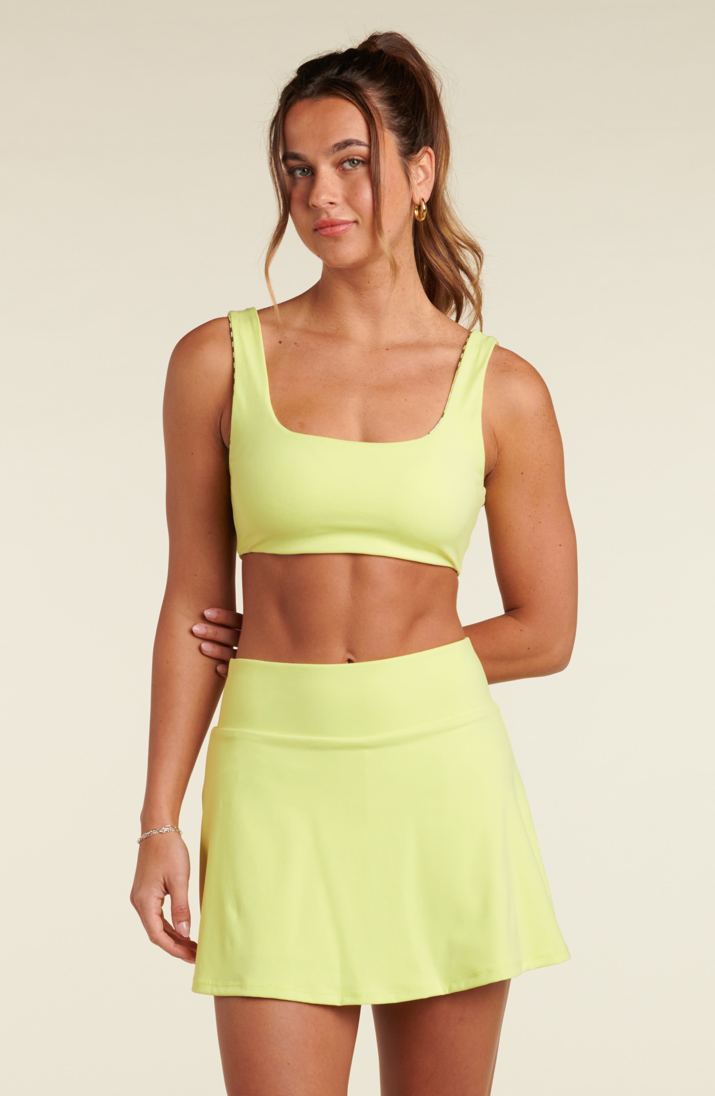 Woman wearing a lime green sports bra and matching skort against a beige background