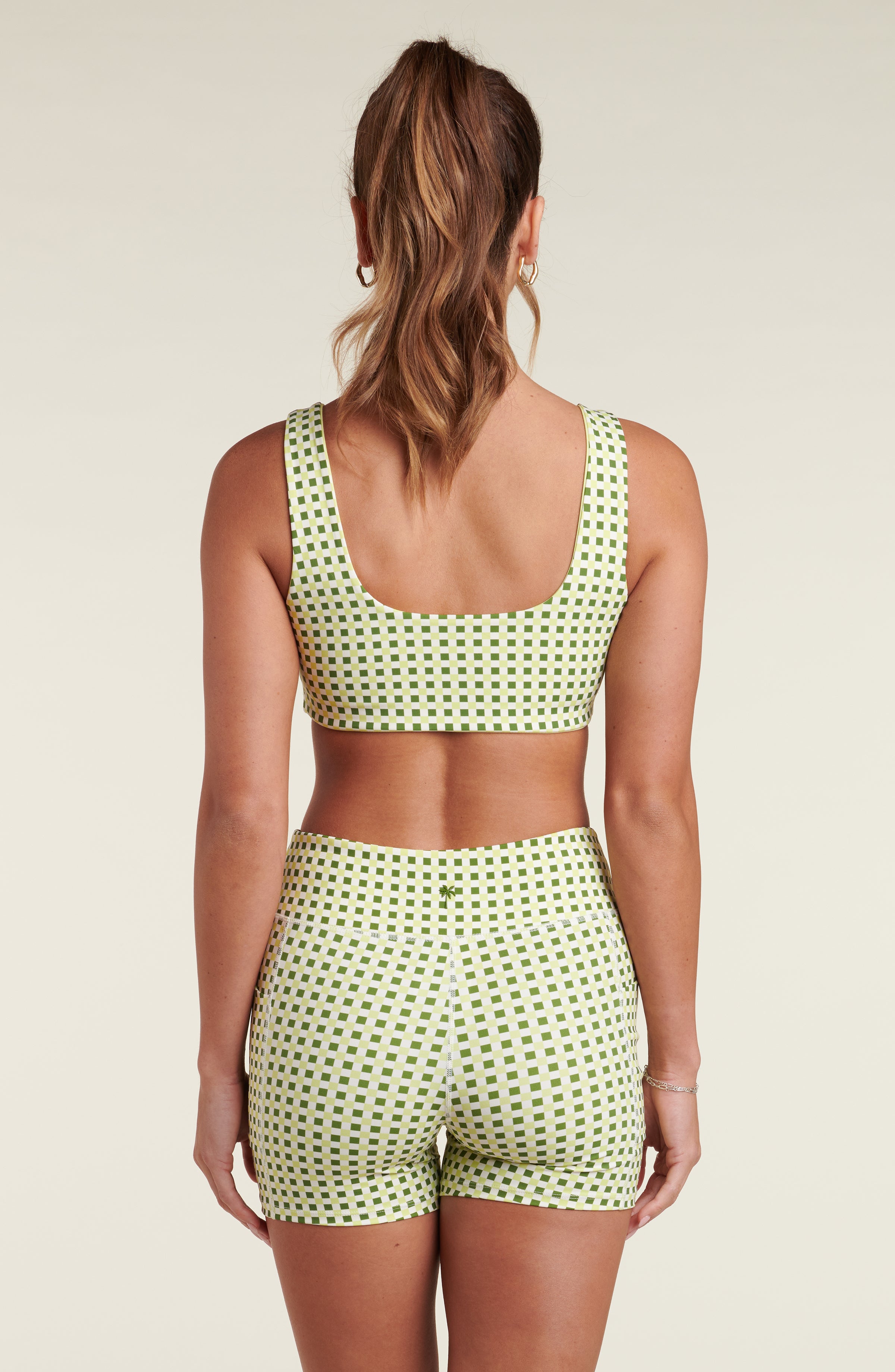 Woman wearing a green patterned sports bra and matching biker shorts against a beige background