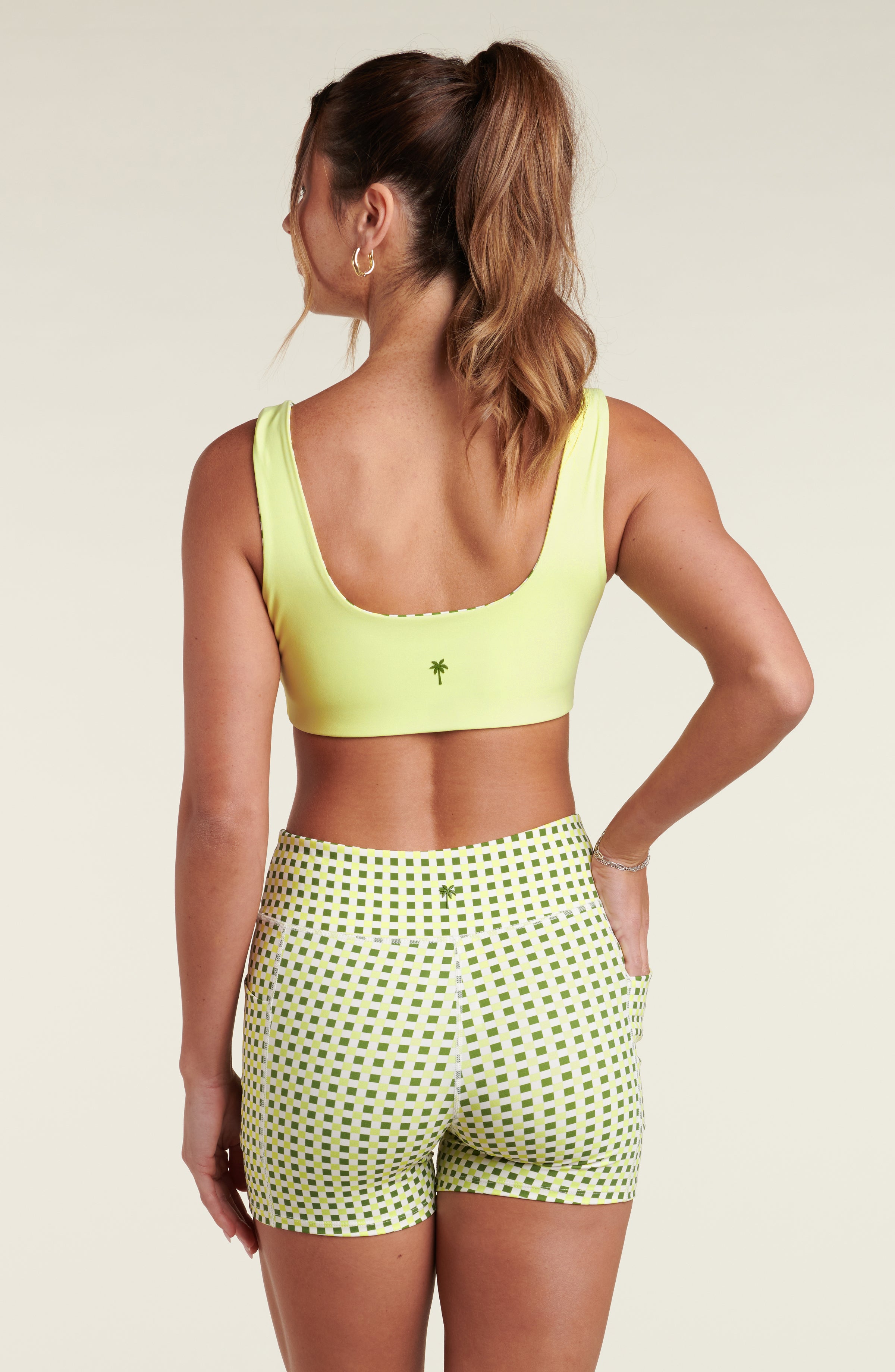 Woman wearing a lime green sports bra and green checkered biker shorts against a beige background