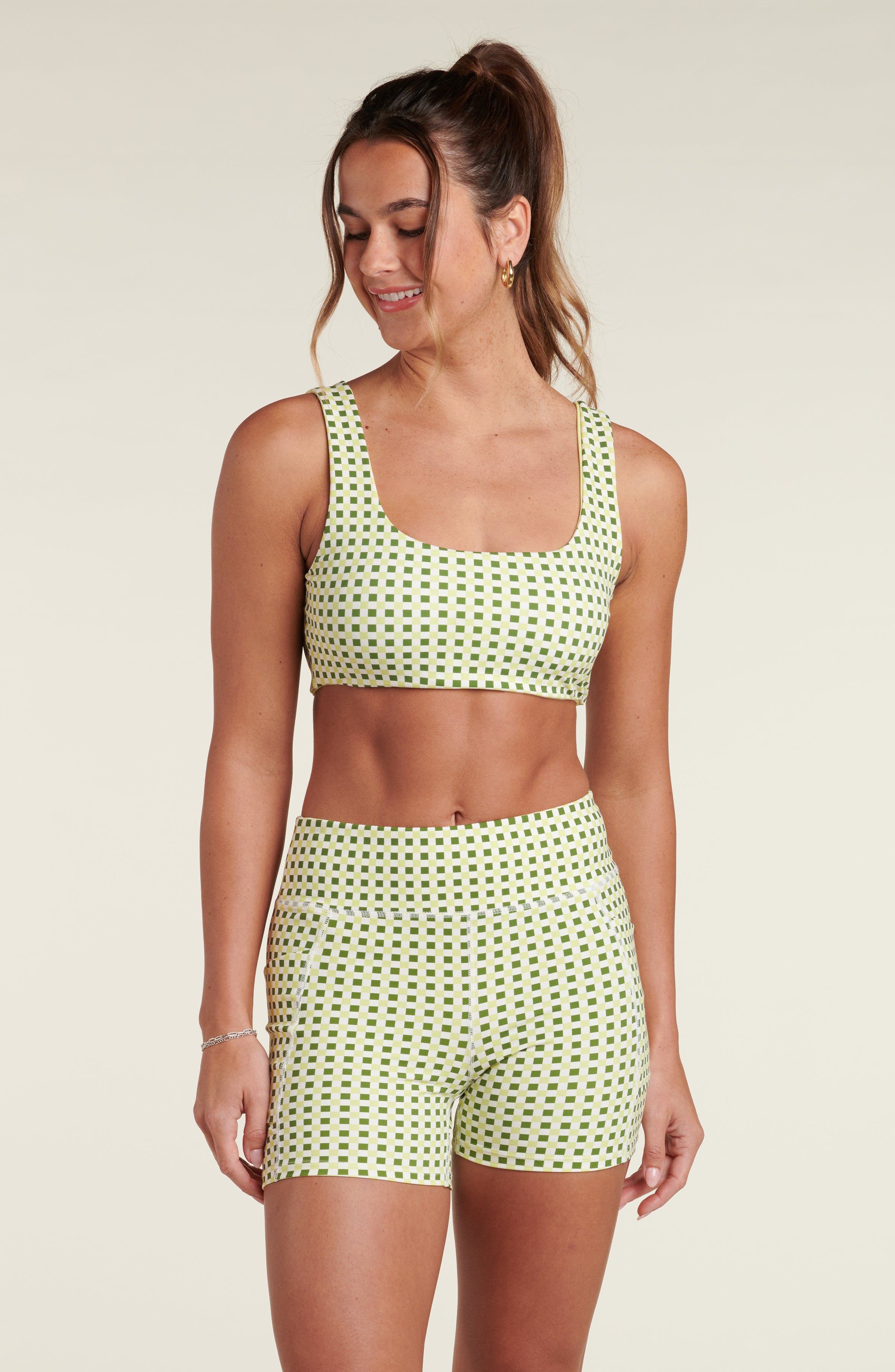 Woman wearing a green patterned sports bra and matching biker shorts against a beige background