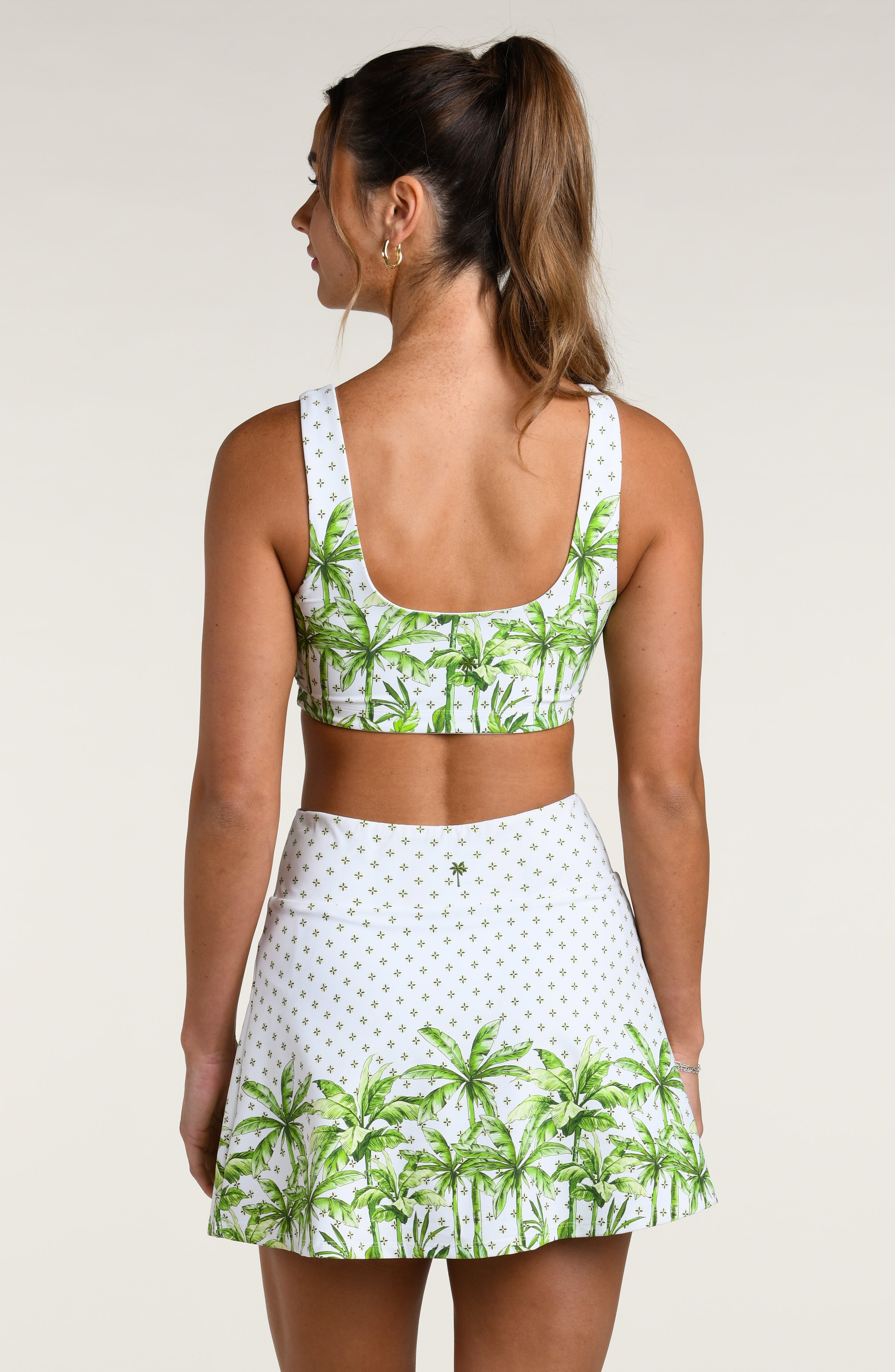 Woman wearing a green palm leaf sports bra and a matching skort on a beige background