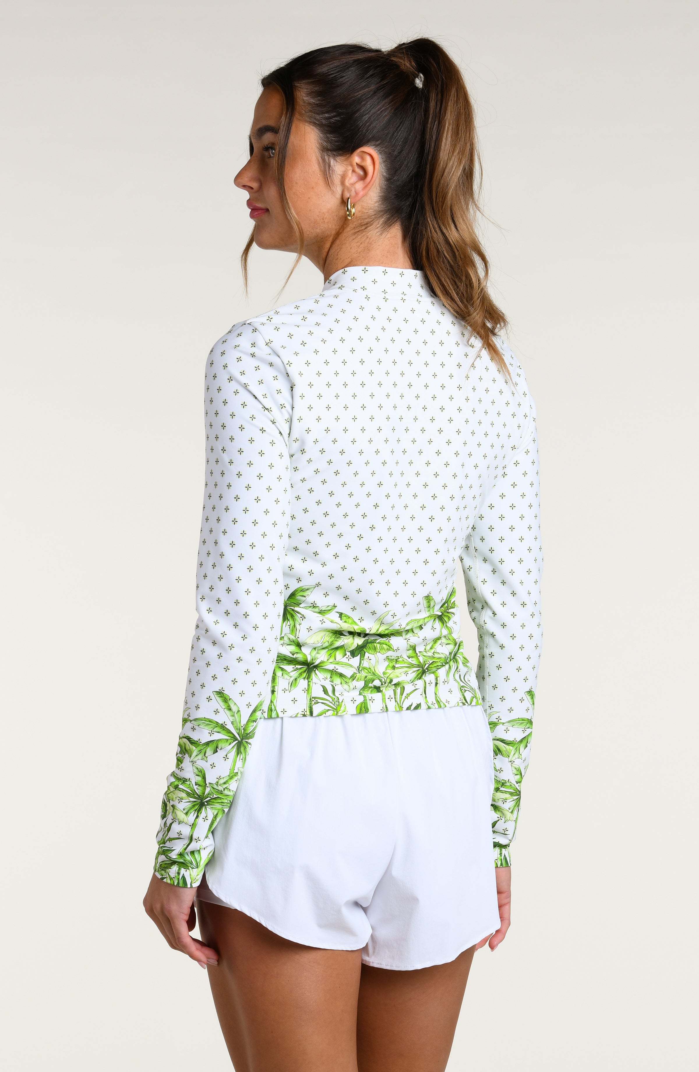 Woman wearing a white long-sleeve top with palm tree design and white shorts on a plain background