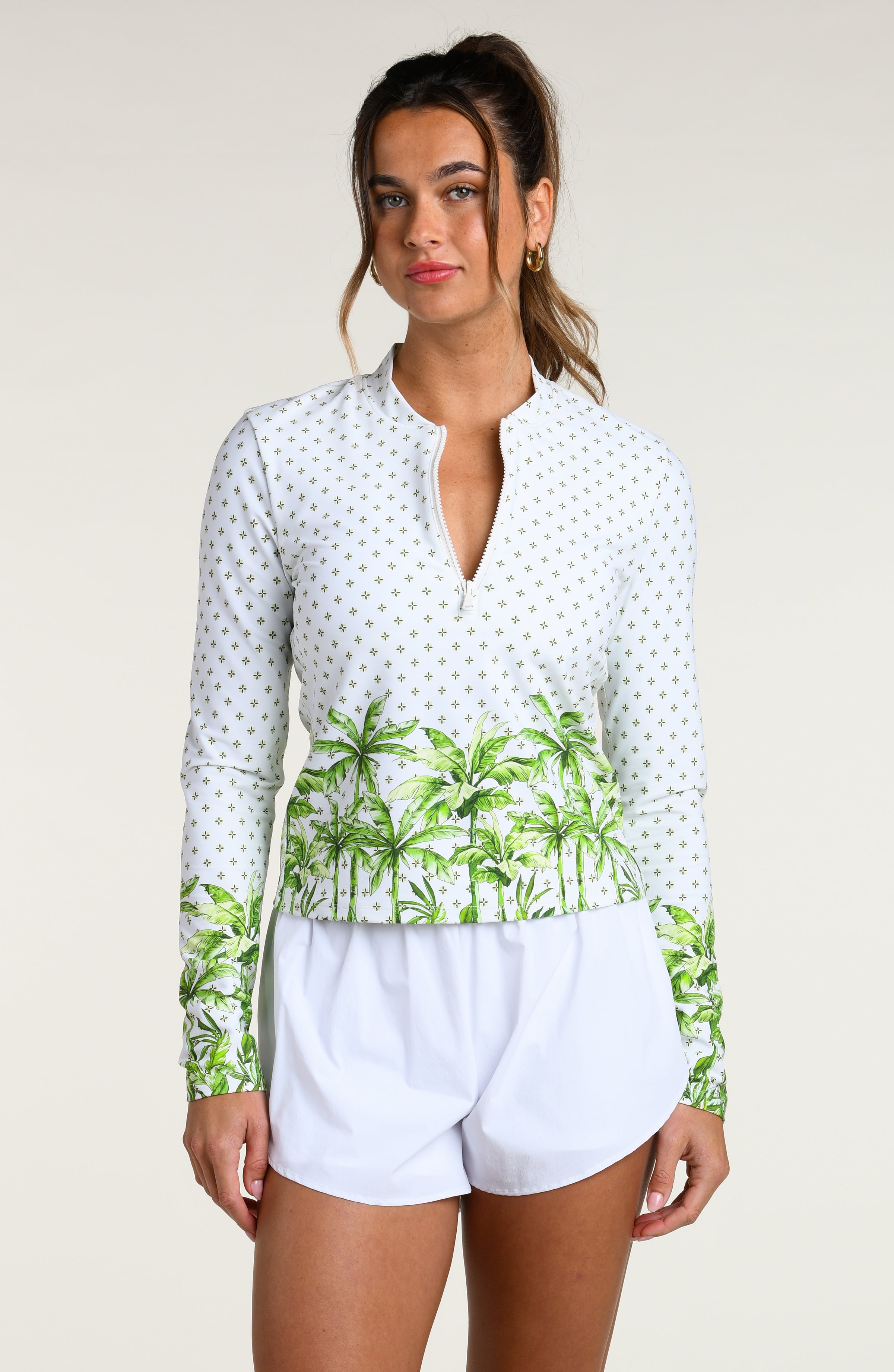 Woman wearing a white long-sleeve top with palm tree design and white shorts on a plain background