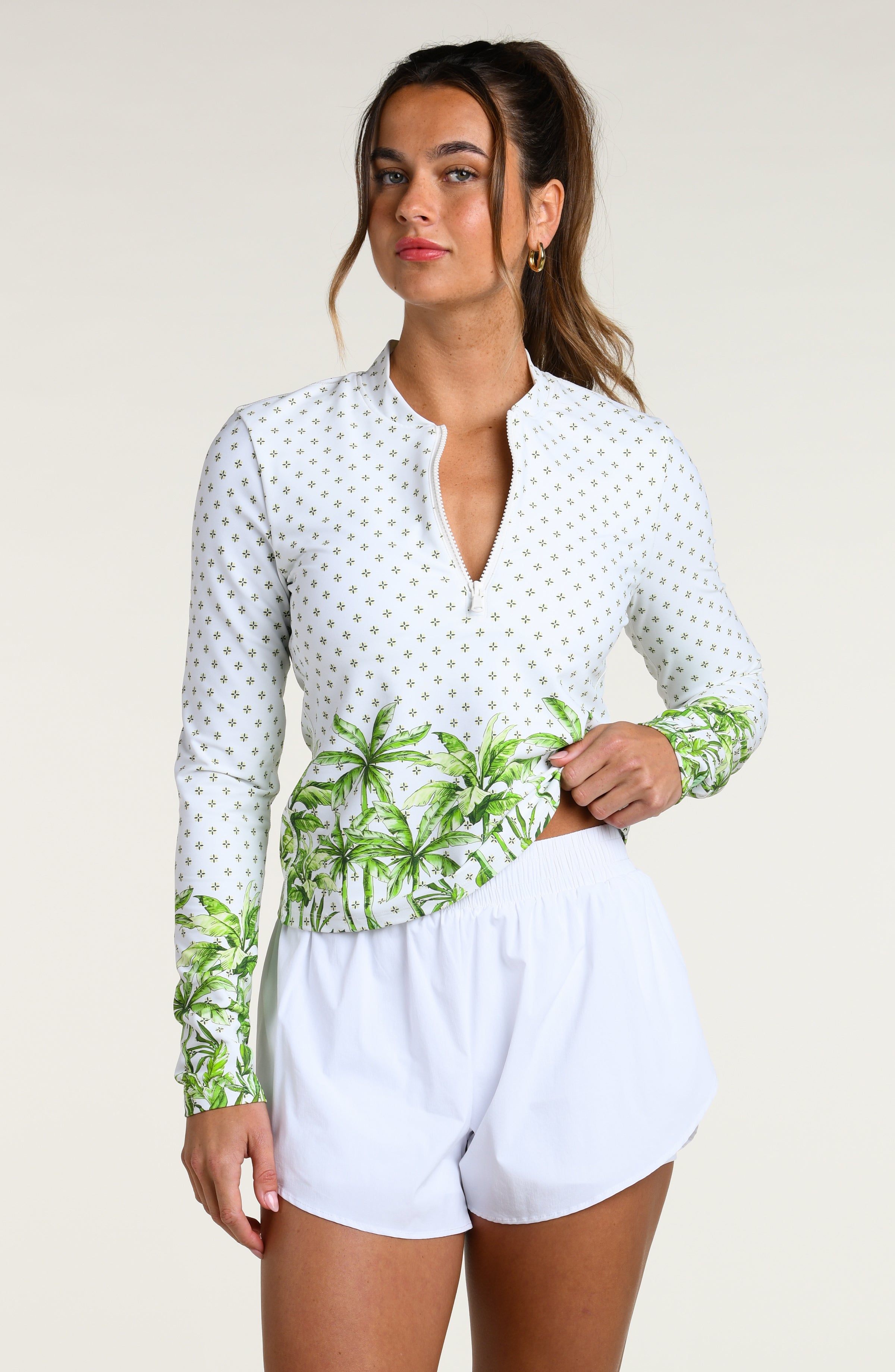 Woman wearing a white long-sleeve top with palm tree design and white shorts on a plain background