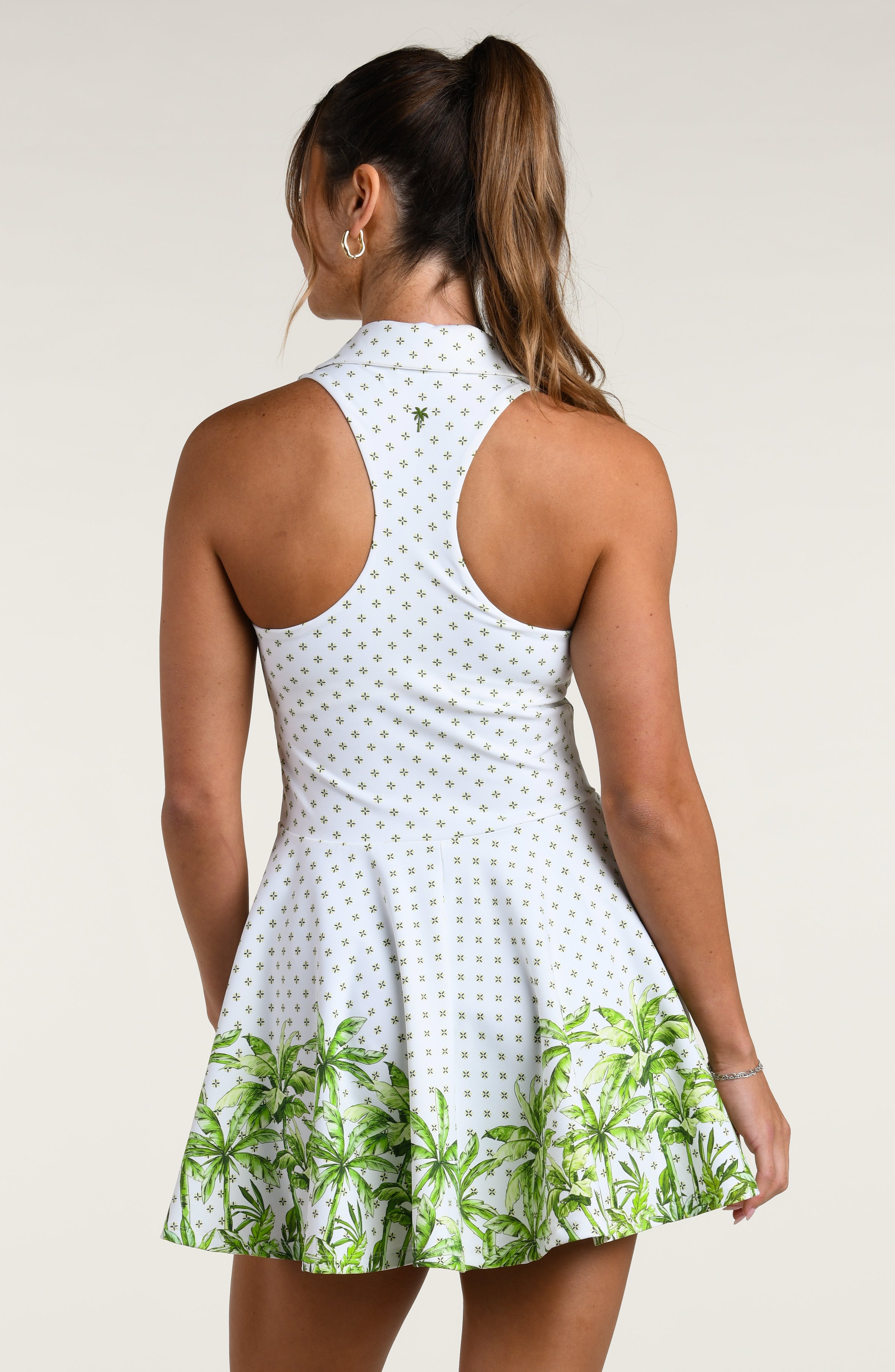Woman wearing a white tennis dress with green palm tree patterns on a plain background