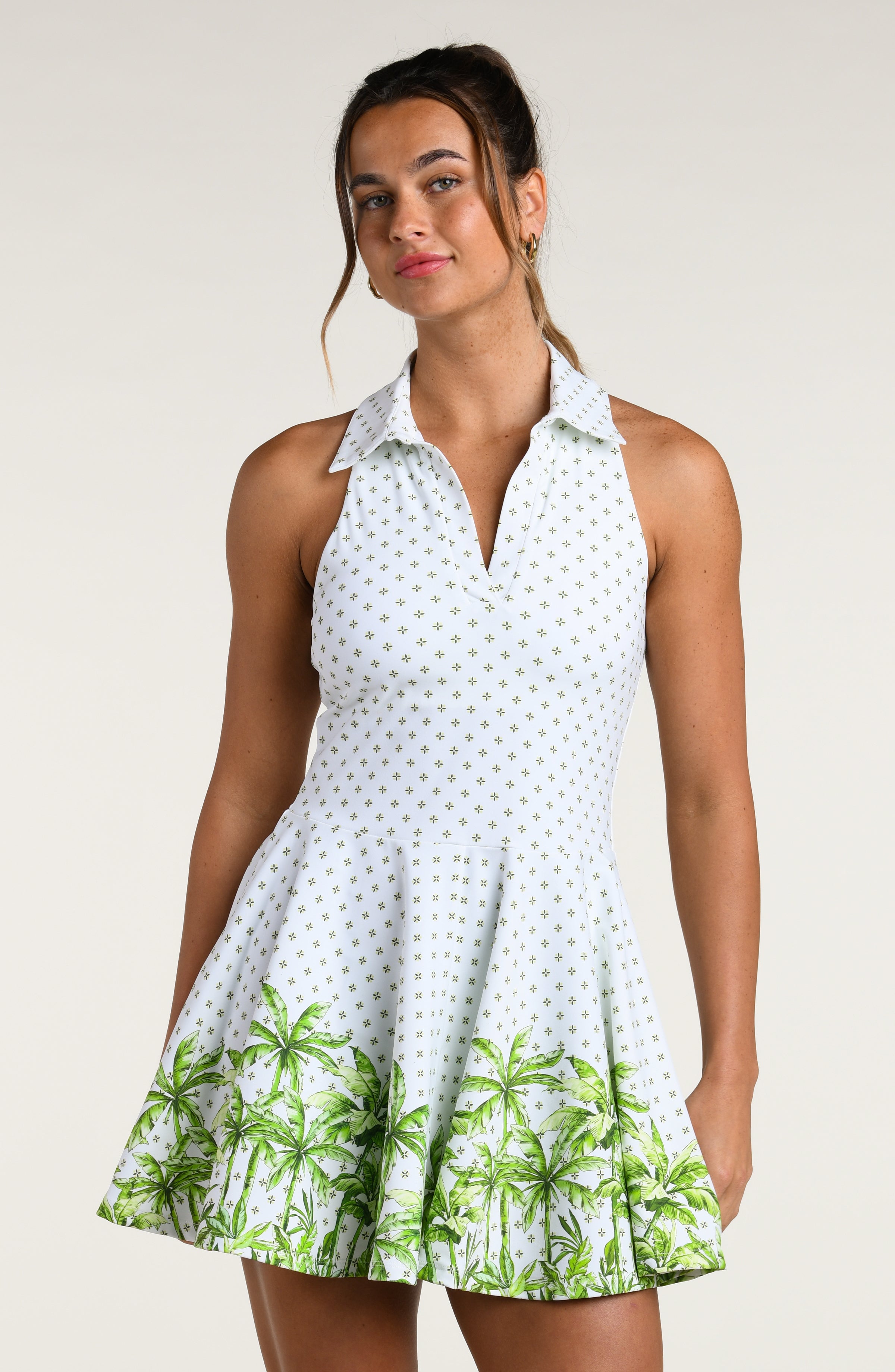 Woman wearing a white tennis dress with green palm tree patterns on a plain background