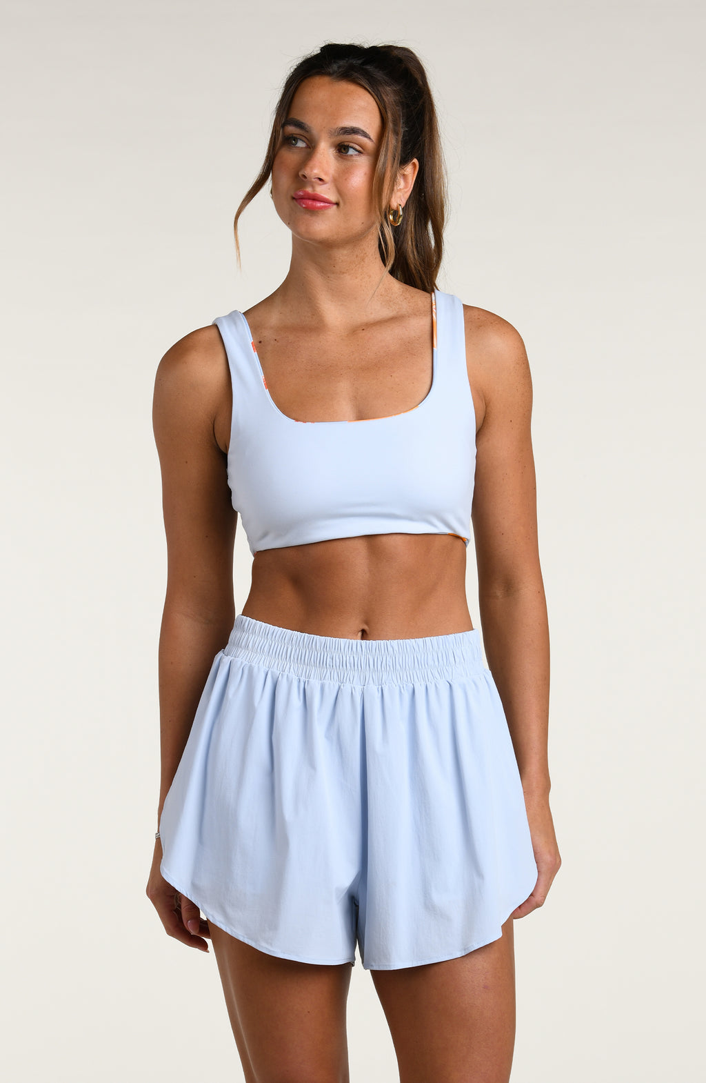 Woman wearing a light blue sports bra and matching running shorts worn by a person against a beige background