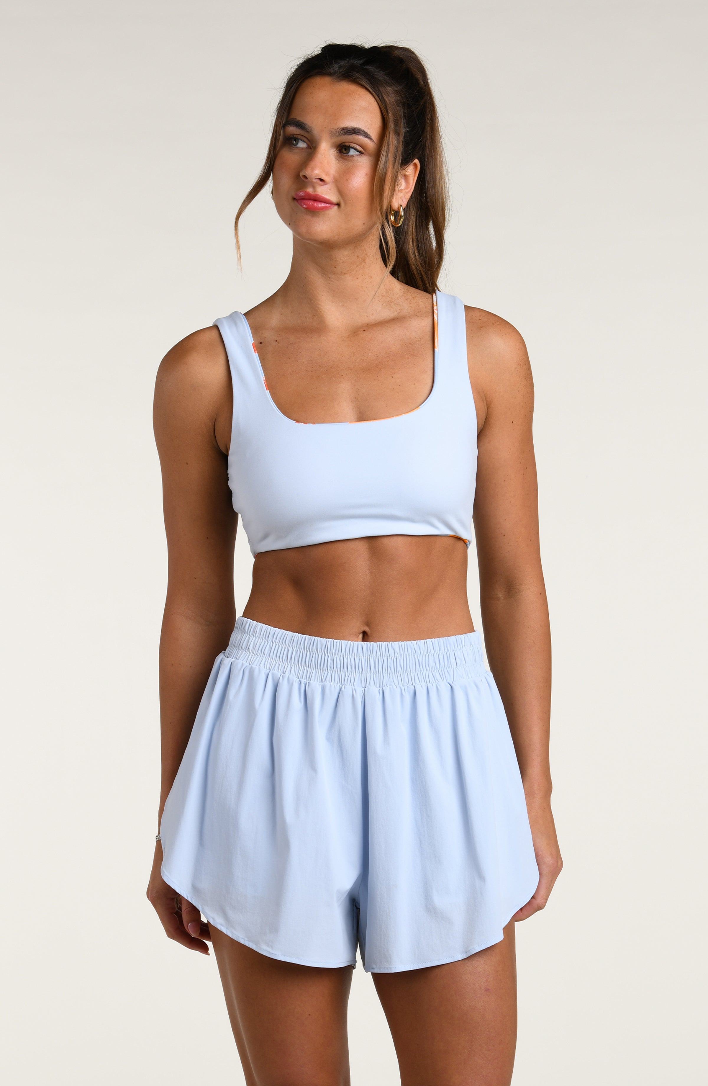 Woman wearing a light blue sports bra and matching running shorts worn by a person against a beige background