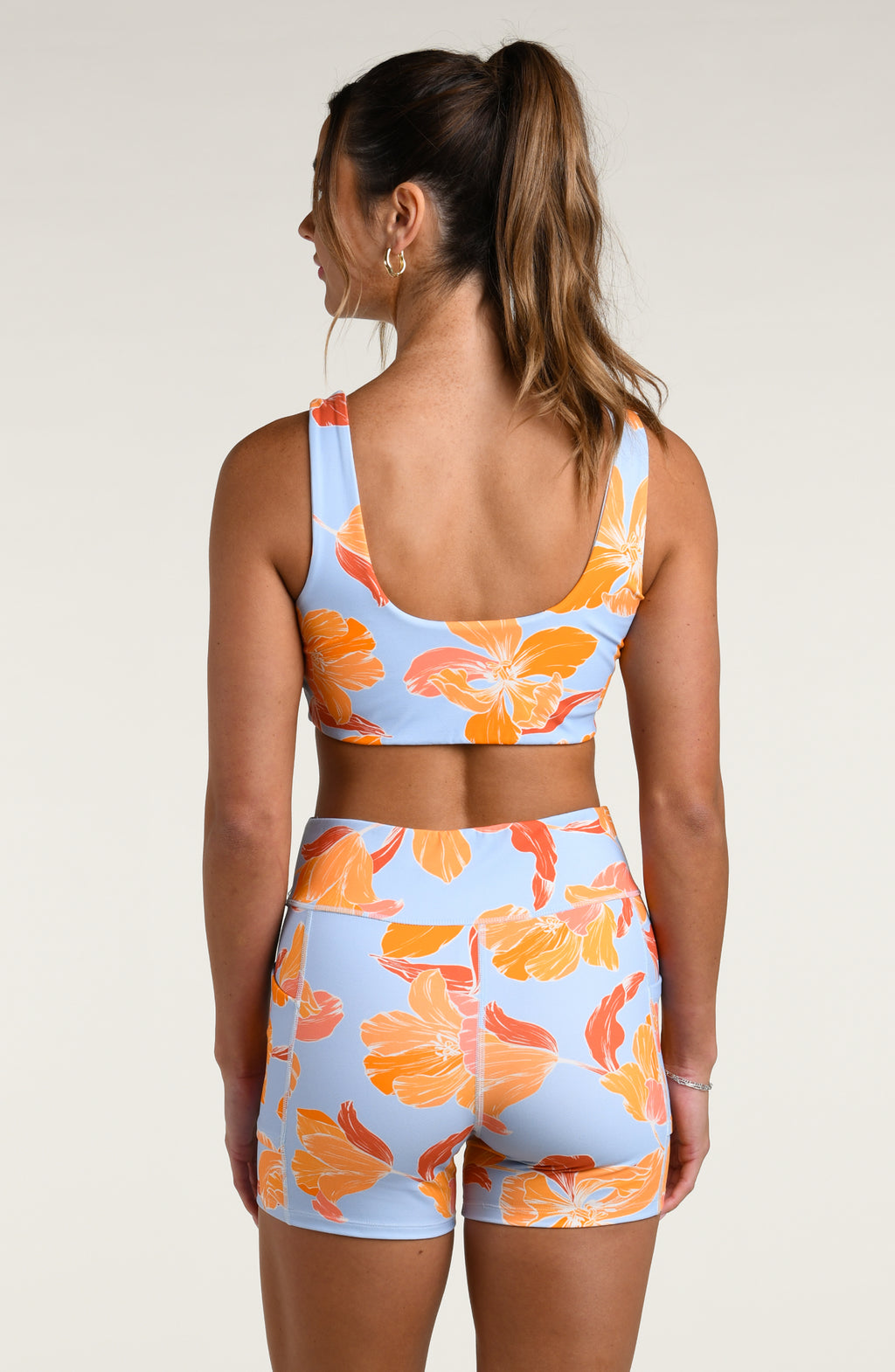 Woman wearing a floral sports bra and matching biker shorts on a plain background