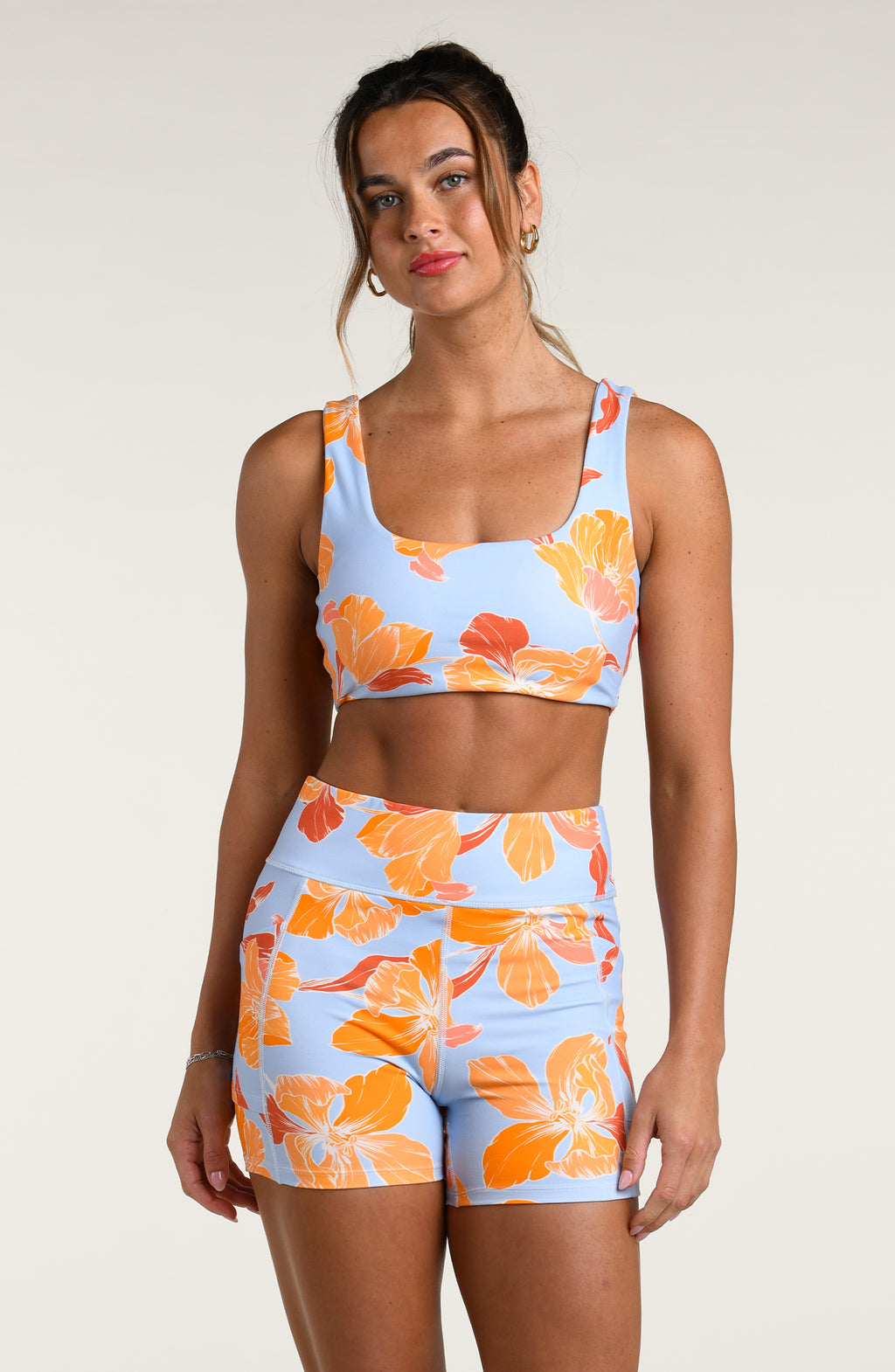 Woman wearing a floral sports bra and matching biker shorts on a plain background