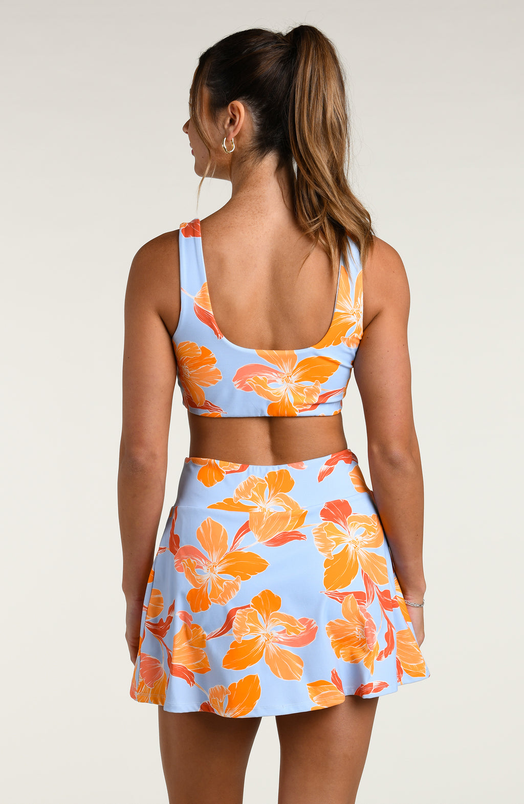 Woman wearing a sports bra and matching skort with orange floral pattern on a light blue background