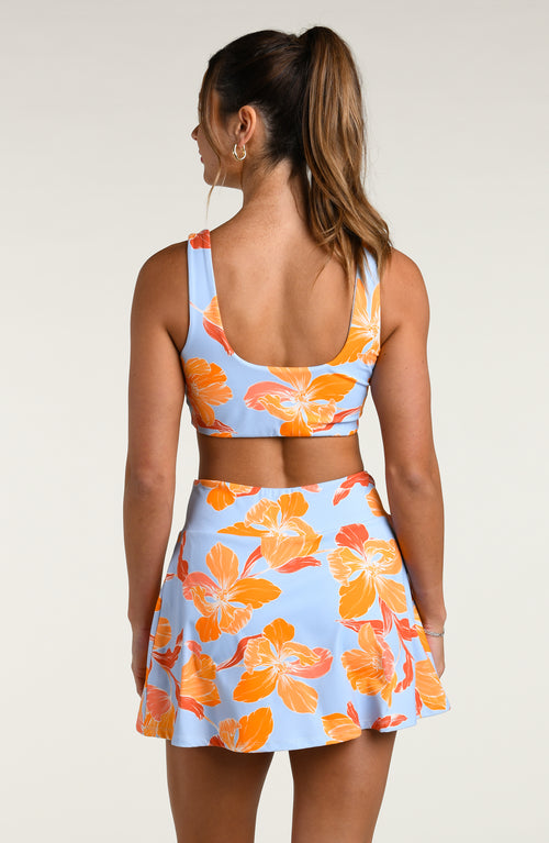 Woman wearing a floral reversible sports bra and matching skort on a plain background