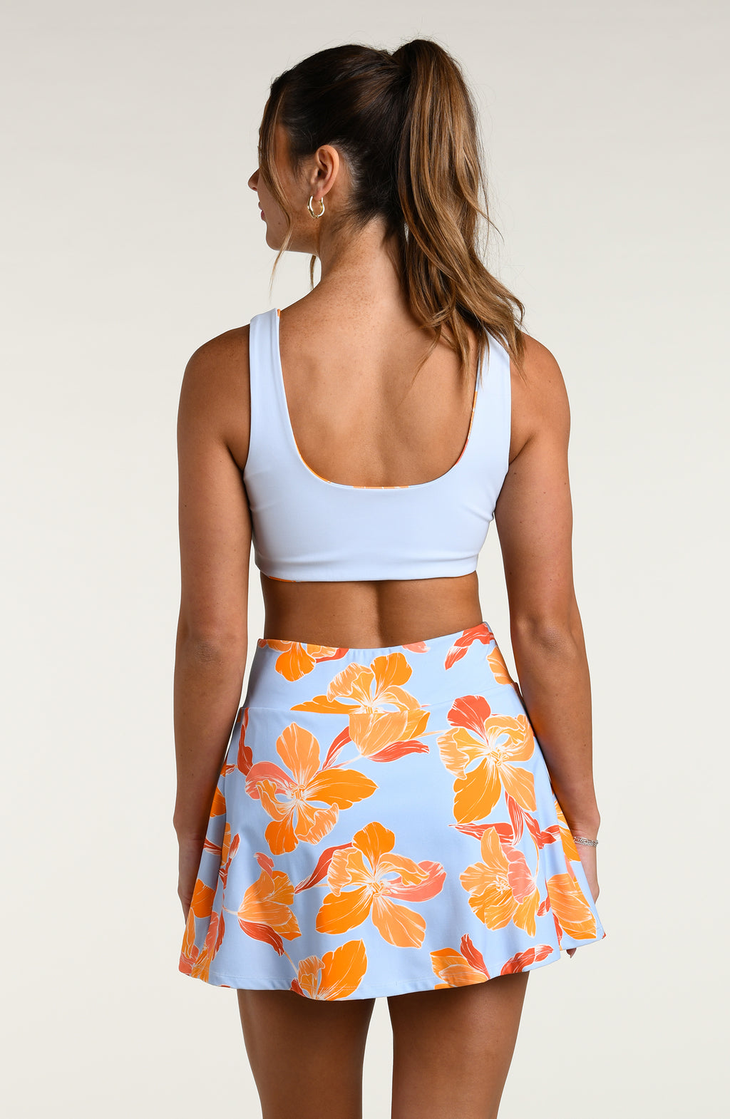Woman wearing a light blue sports bra and floral skort against a white background. 