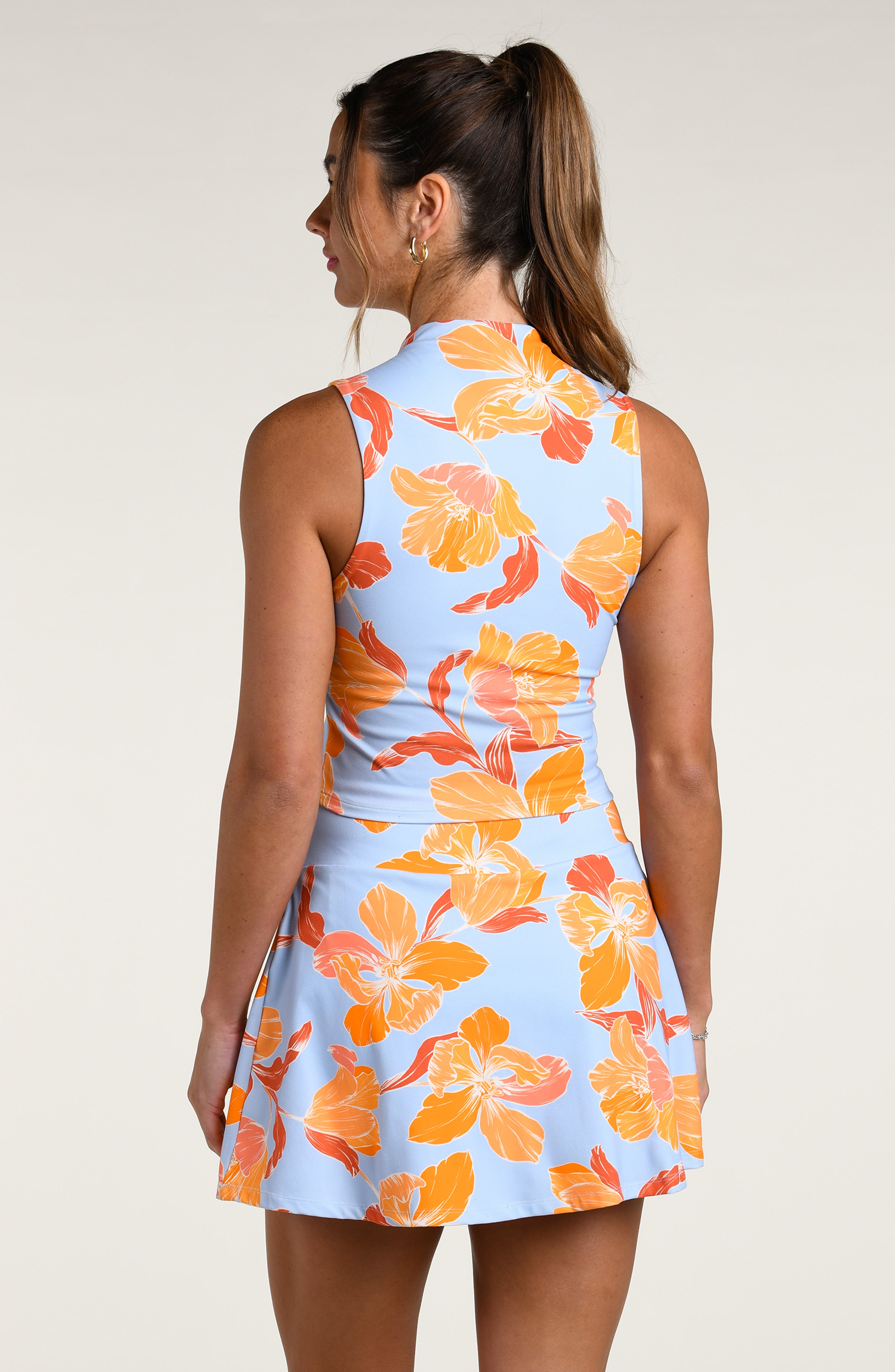 Woman wearing a sleeveless top and matching skort with orange floral pattern on a light blue background