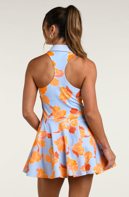 Woman wearing a floral tennis dress with orange flowers on a light blue background