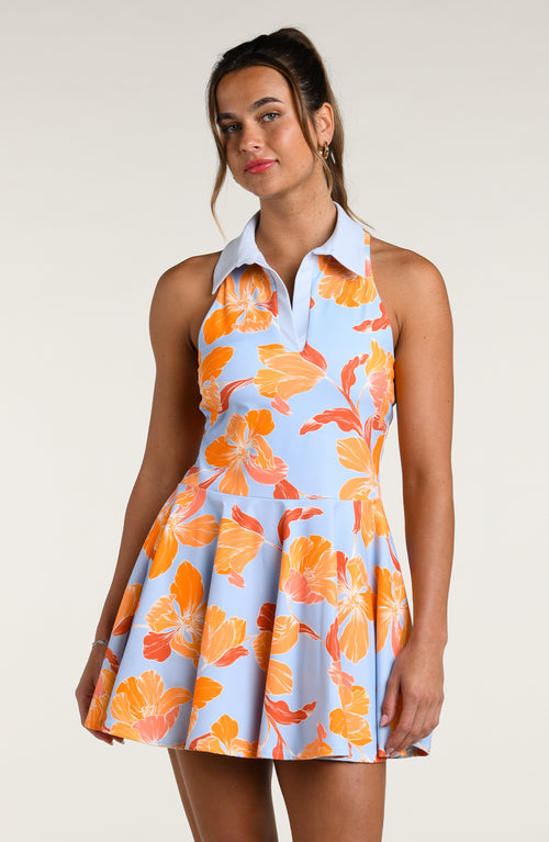 Woman wearing a floral tennis dress with orange flowers on a light blue background