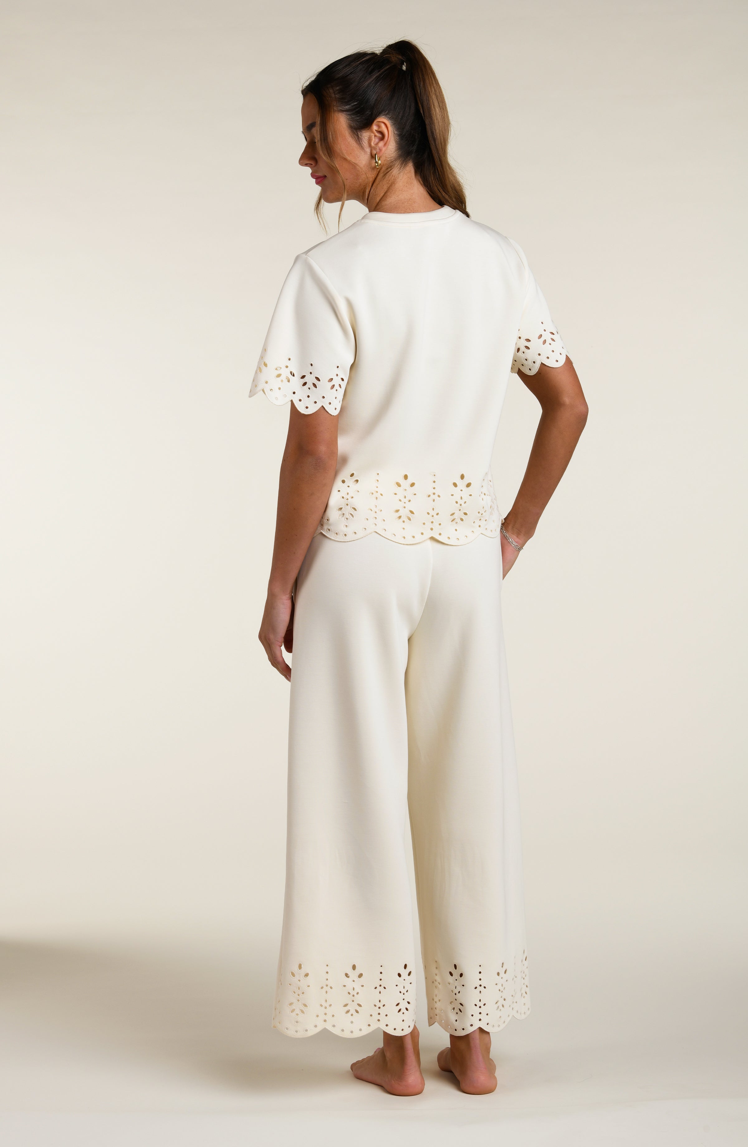 Woman wearing a beige short sleeve top with scalloped edges and a matching pants on a plain background