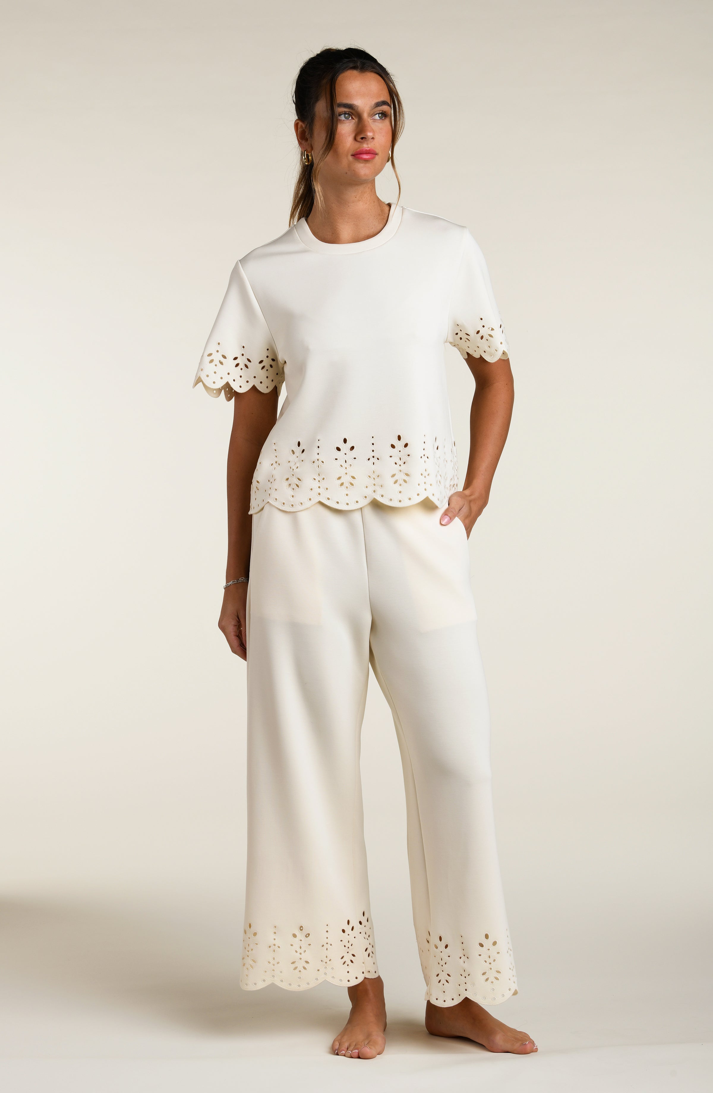 Woman wearing a beige short sleeve top with scalloped edges and matching pants on a plain background