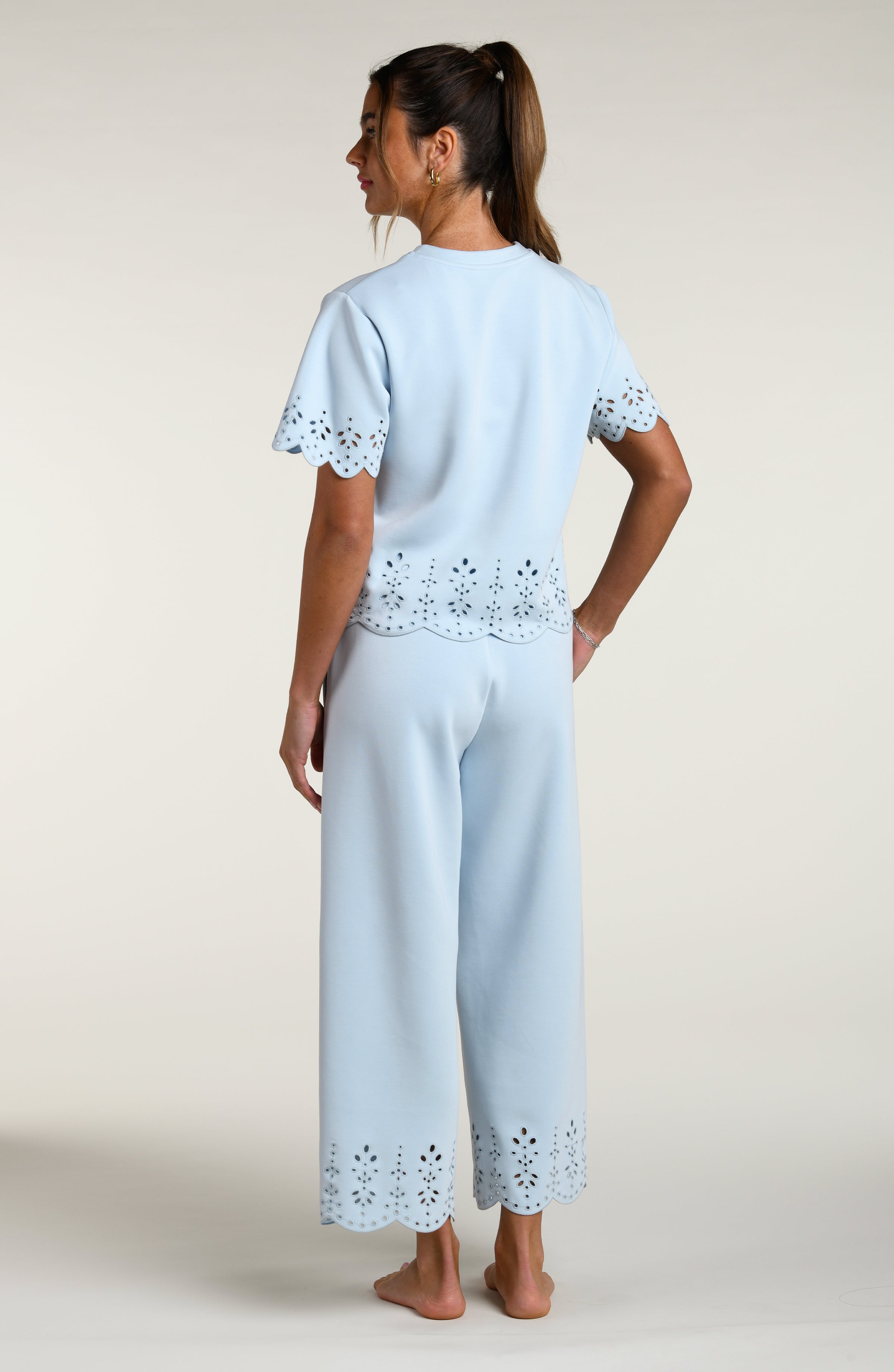 Woman wearing a light blue short sleeve top with scalloped edges and matching pants on a plain background