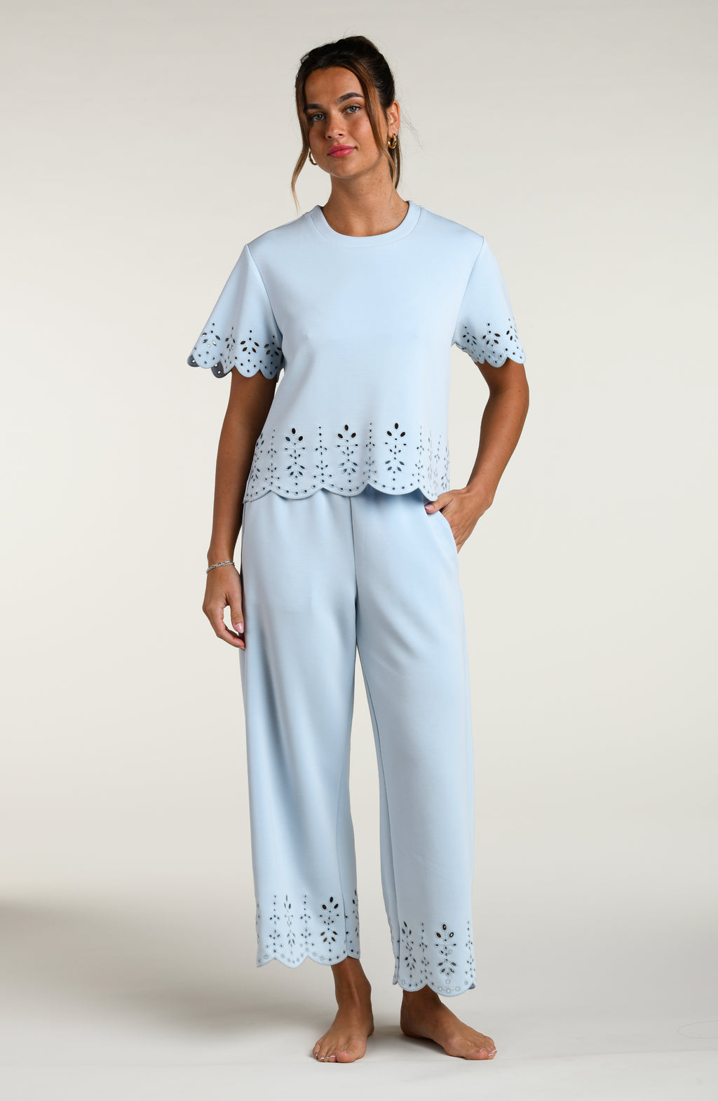 Woman wearing a light blue short sleeve top with scalloped edges and a matching pants on a plain background