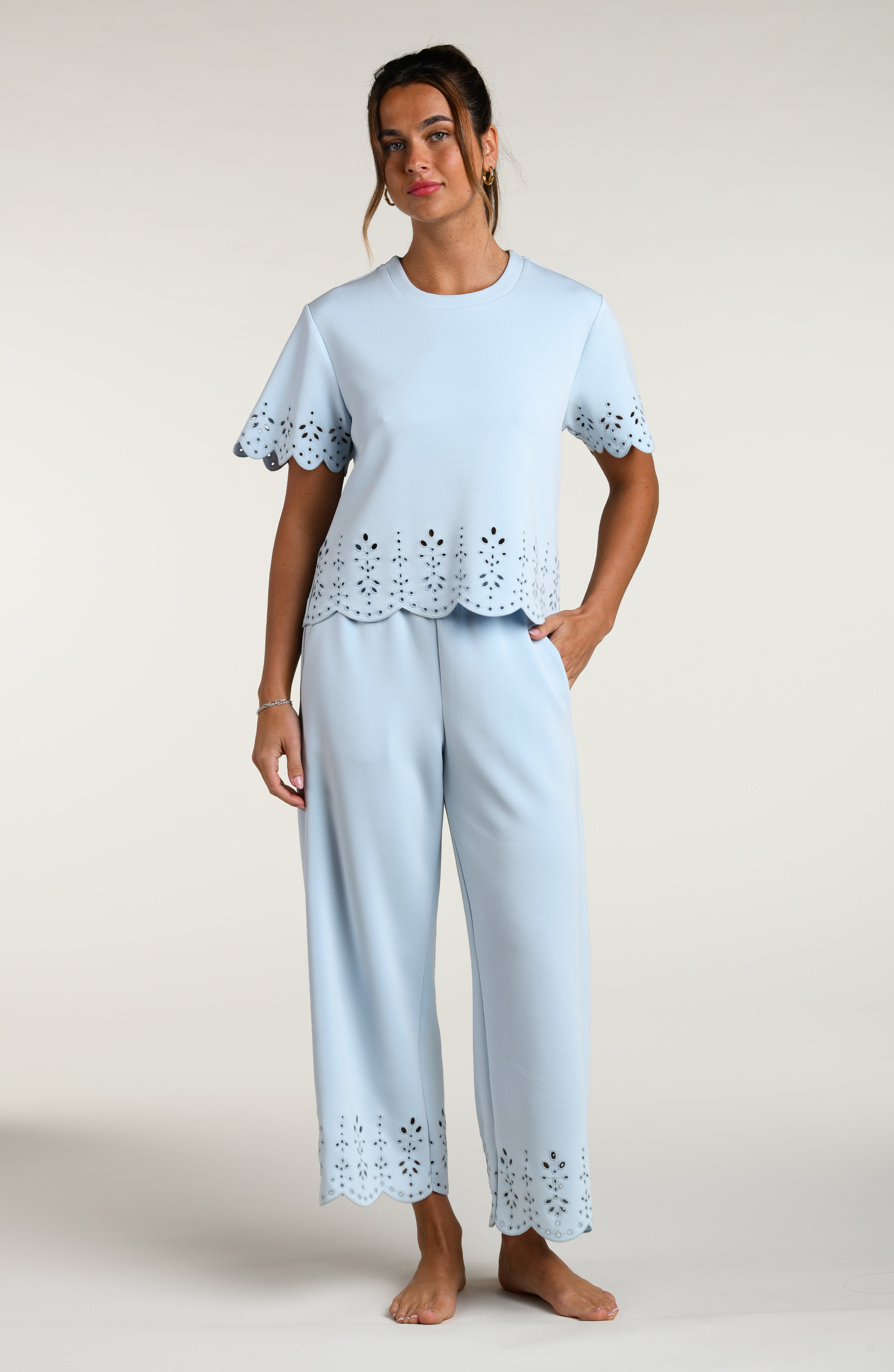 Woman wearing a light blue short sleeve top with scalloped edges and a matching pants on a plain background