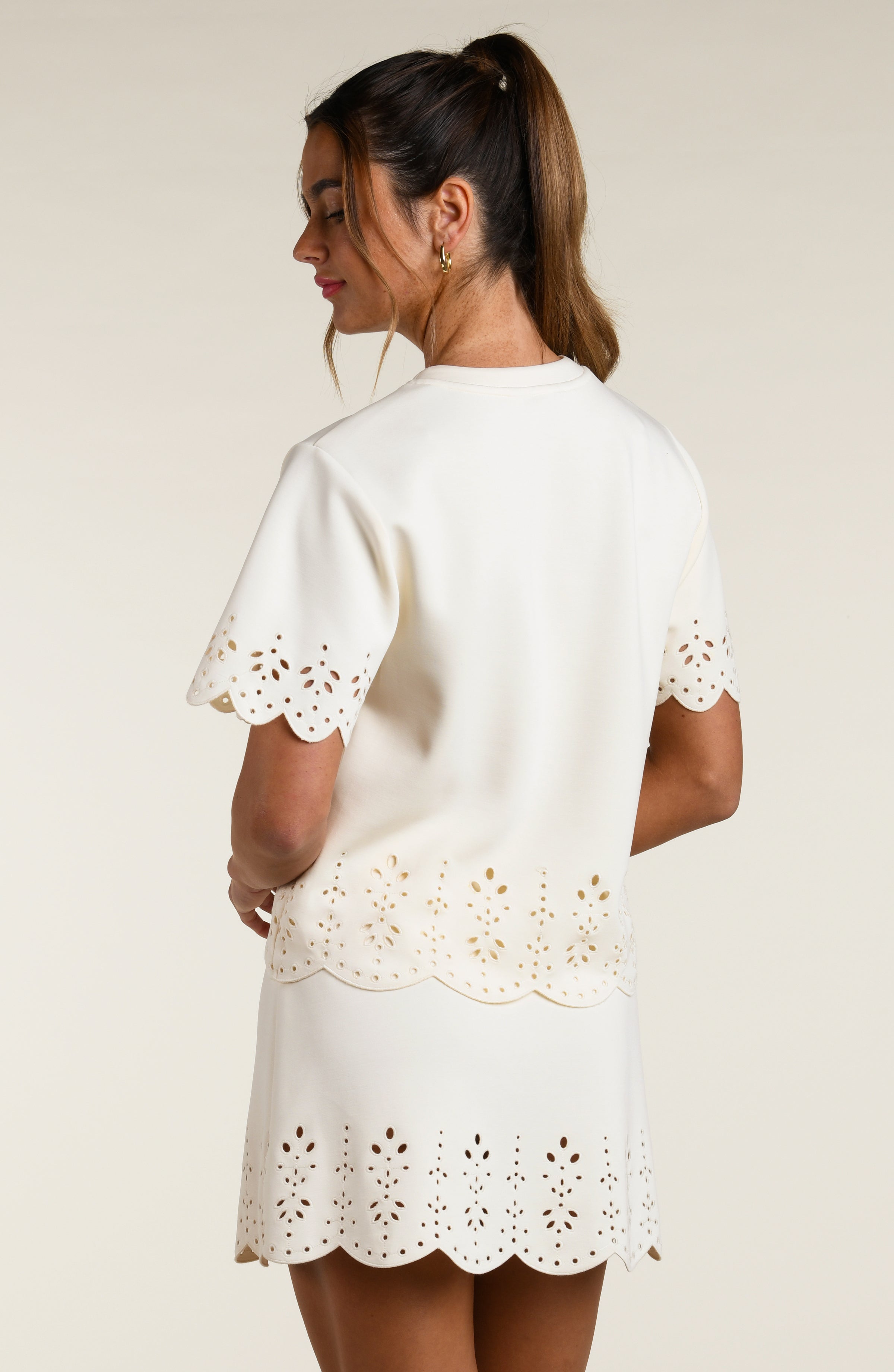 Woman wearing a beige short sleeve top with scalloped edges and a matching skirt on a plain background