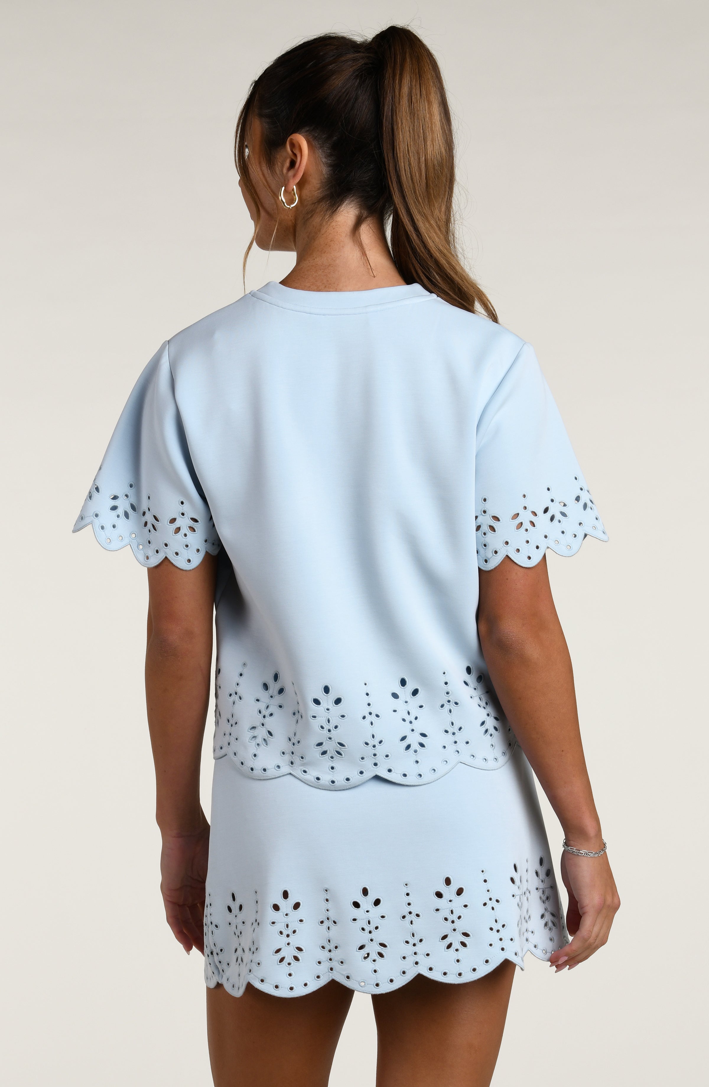 Woman wearing a light blue short sleeve top with scalloped edges and a matching skirt on a plain background